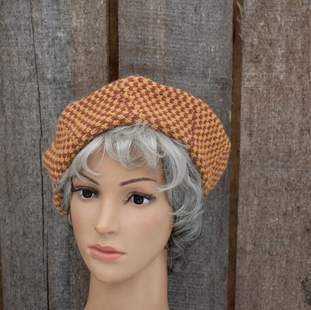 Mannequin head wearing a brown checkered beret against a wooden background
