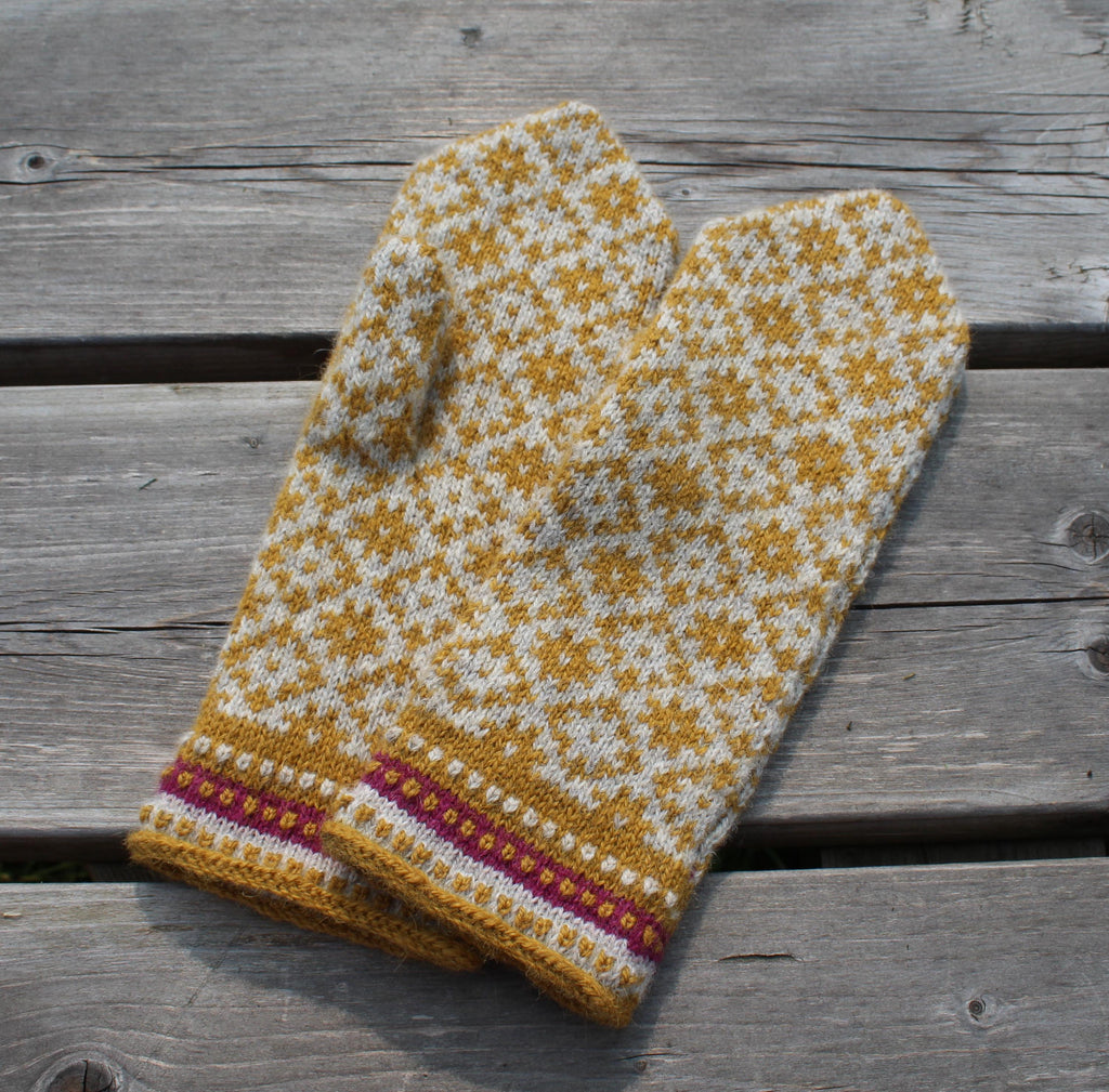 Pair of knitted mittens with a yellow and white pattern on a wooden surface