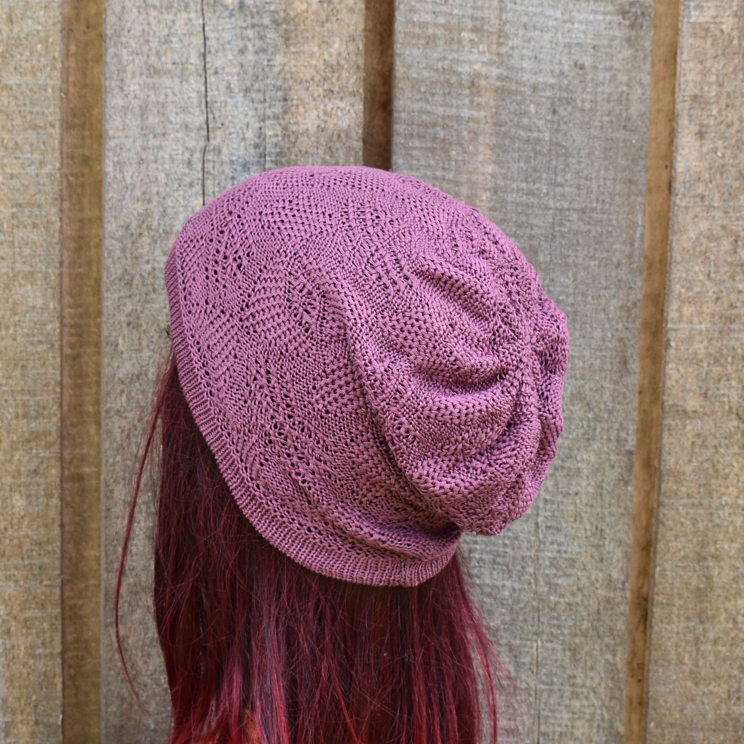 Purple knitted beanie on a person with red hair against a wooden background