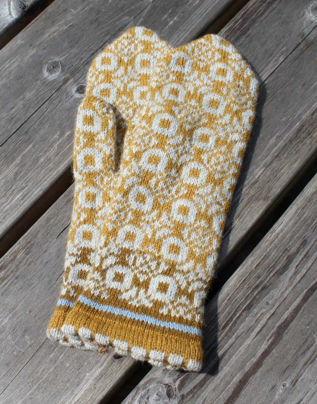 Knitted mittens with a yellow and white pattern on a wooden surface