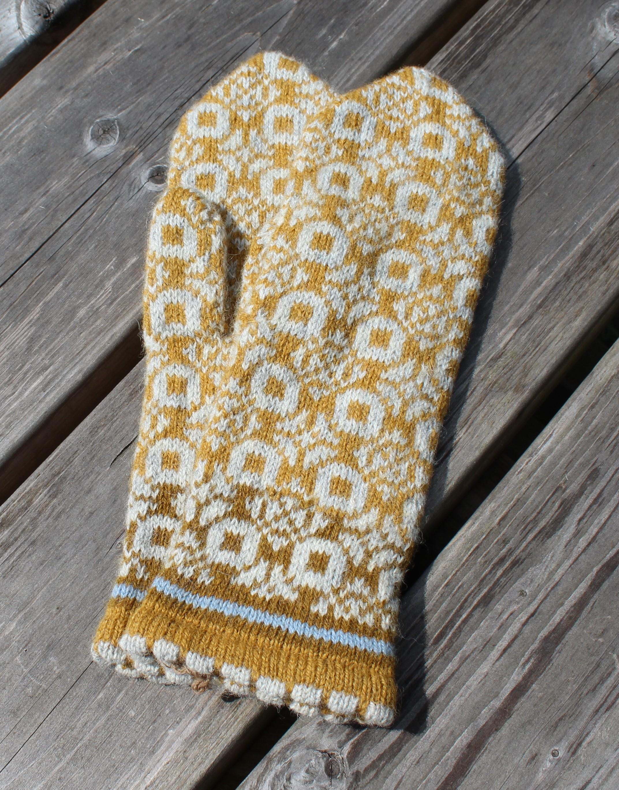 Knitted mittens with a yellow and white pattern on a wooden surface