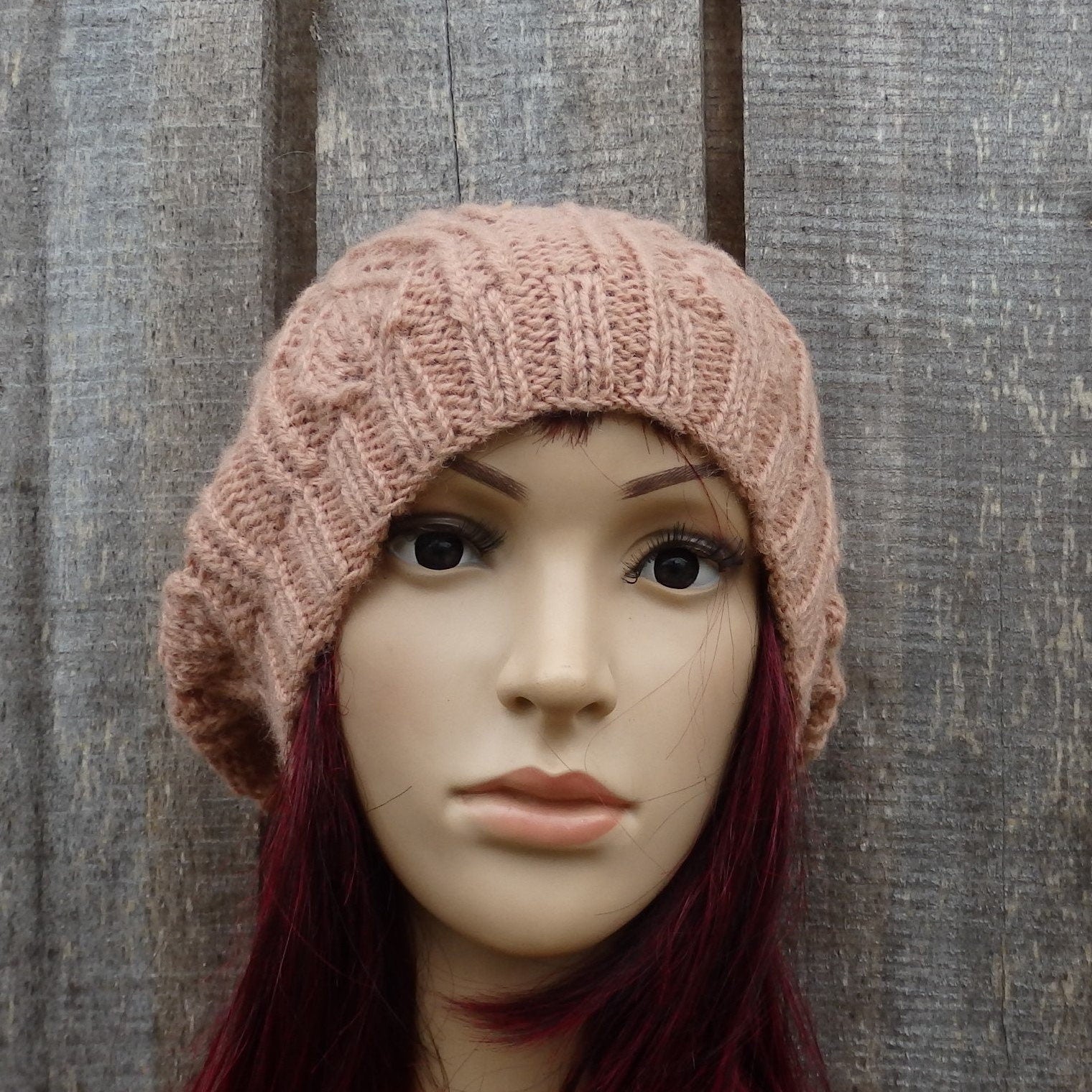 Mannequin head wearing a pink knitted hat against a wooden background