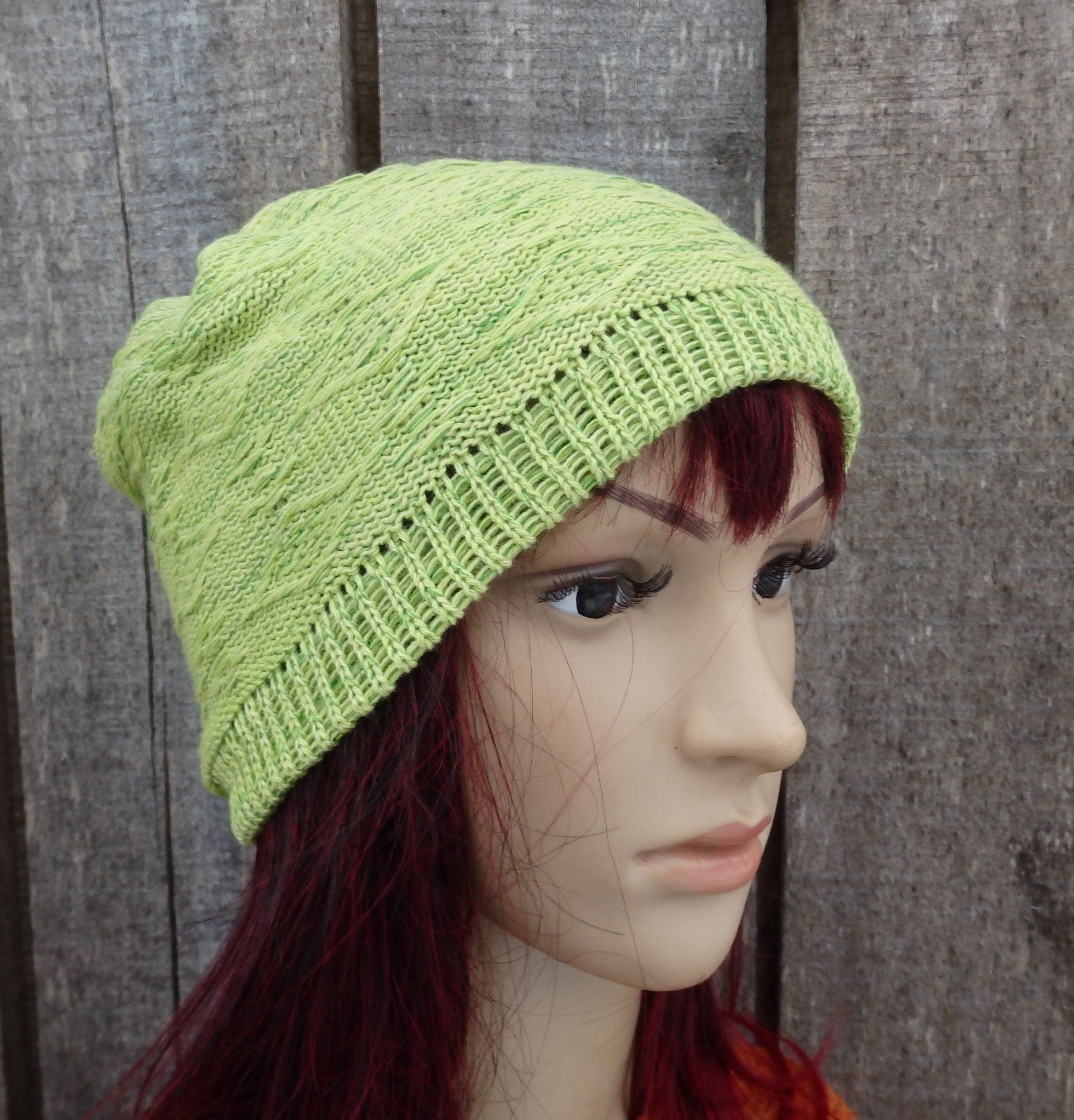 Green knitted beanie on a mannequin head against a wooden background