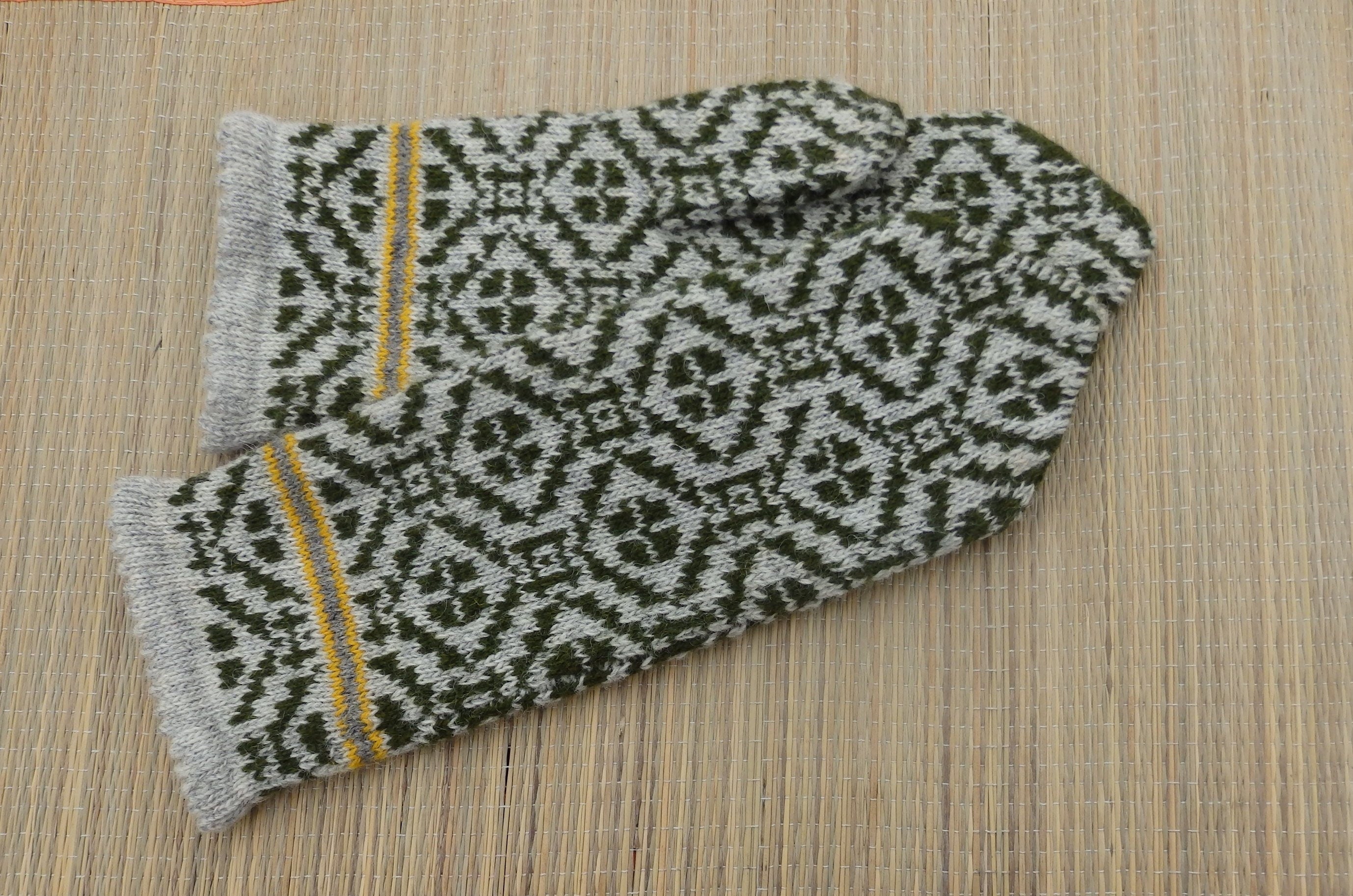 Pair of knitted mittens with a geometric pattern on a wooden surface
