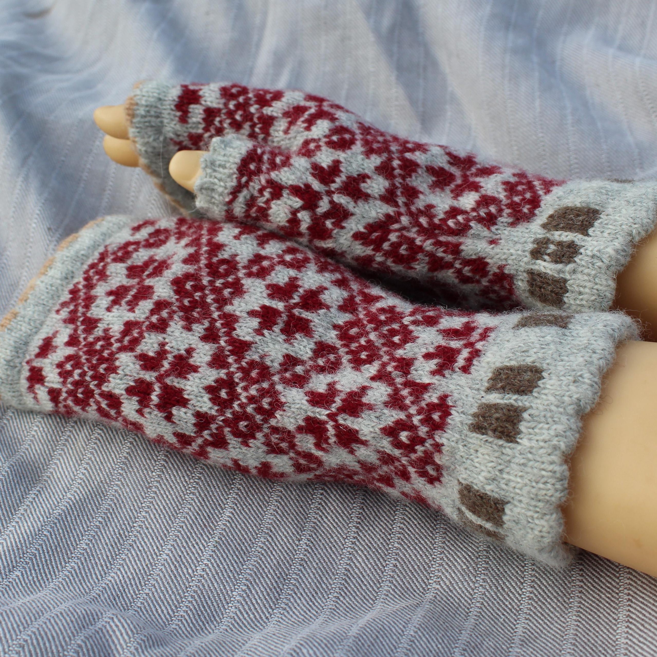 Pair of red and gray patterned mittens on a light blue fabric background