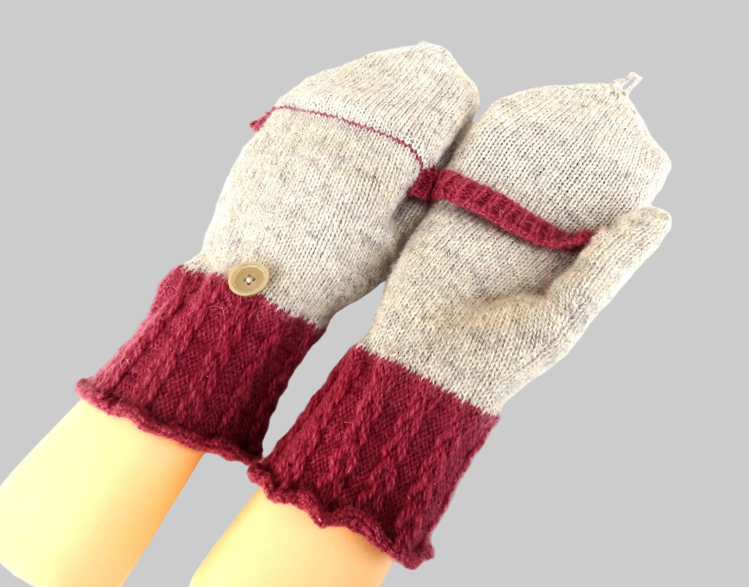 Pair of knitted mittens with red cuffs and buttons on a white background