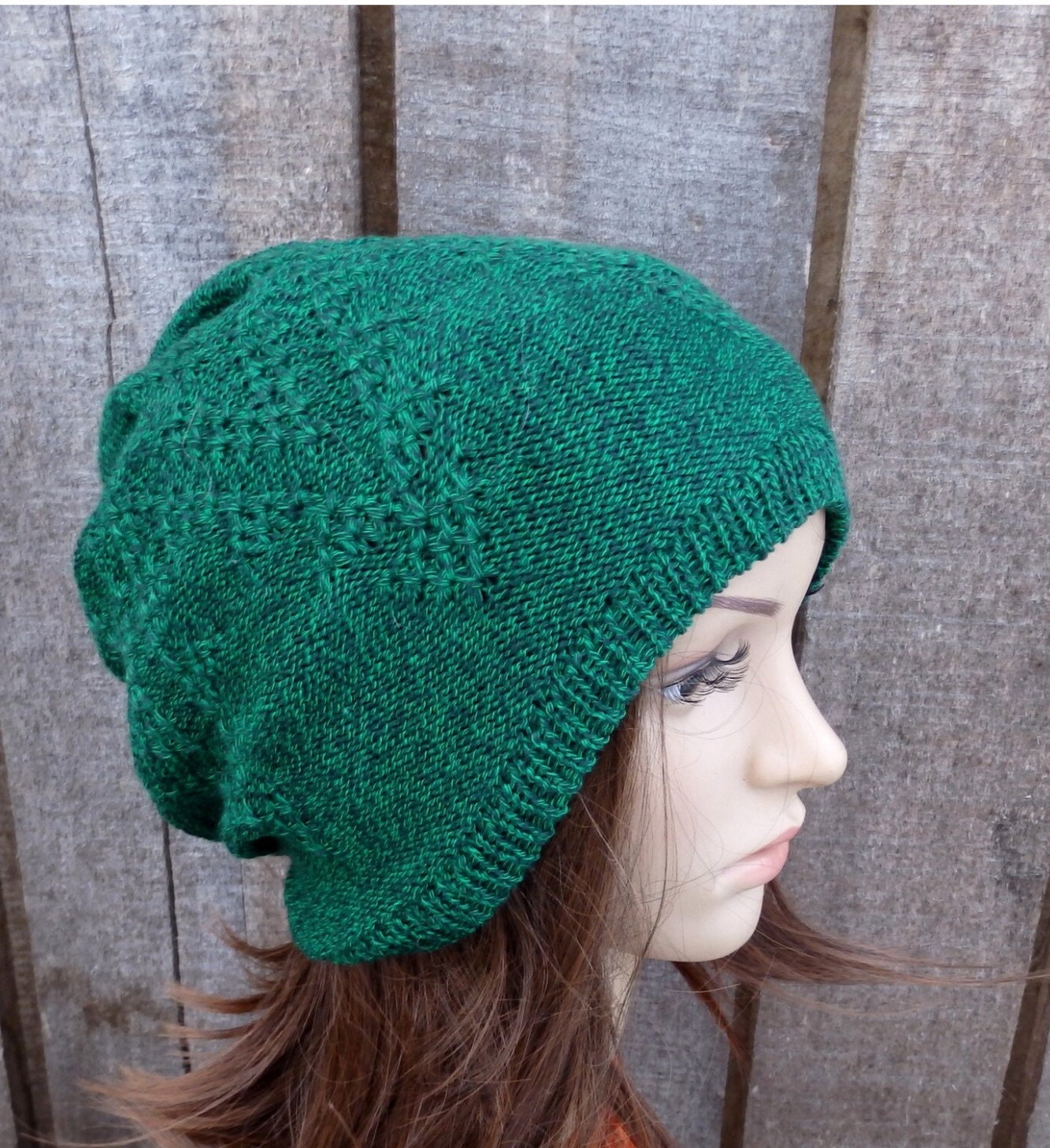 Green knitted beanie worn by a person against a wooden background