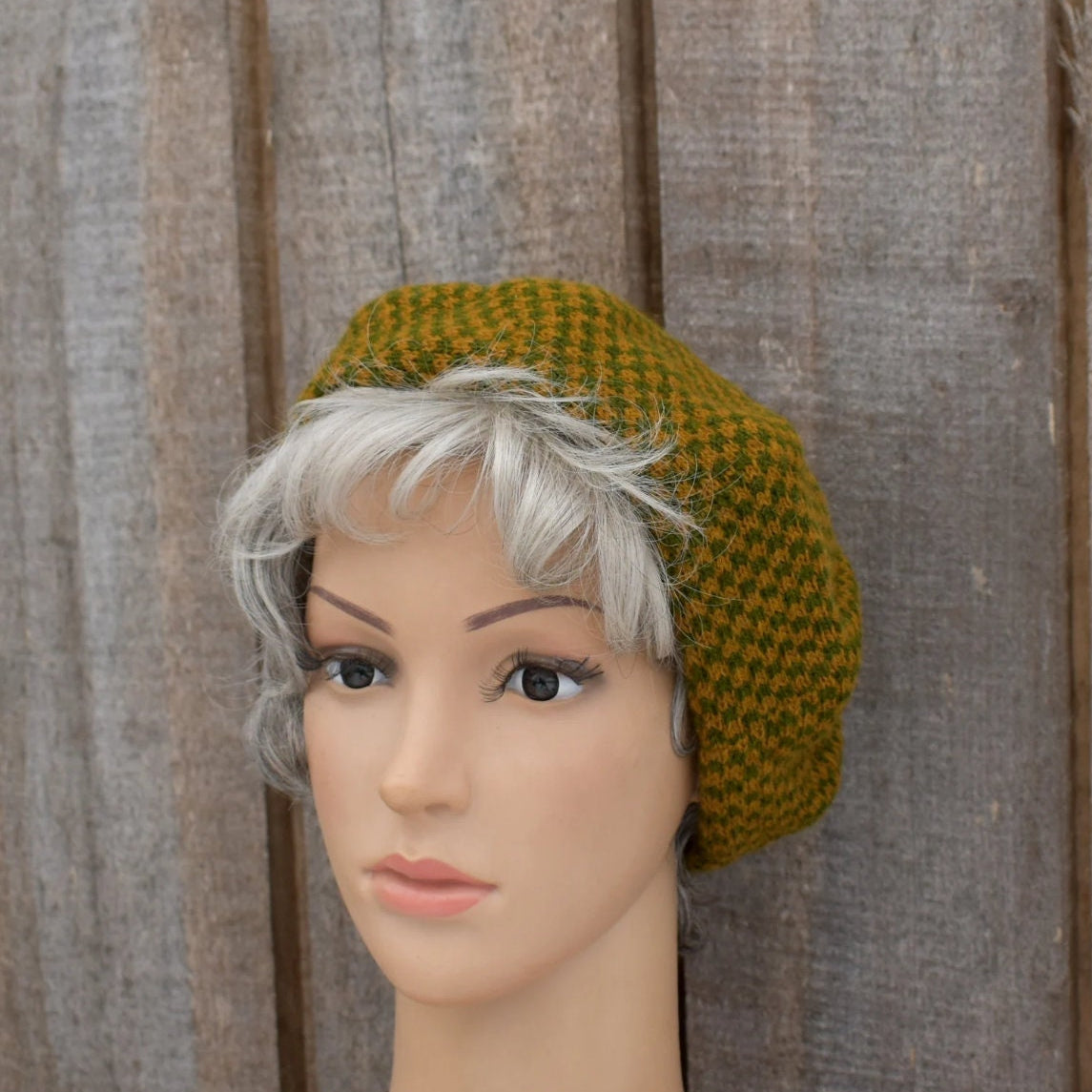 Mannequin head wearing a green knitted hat against a wooden background