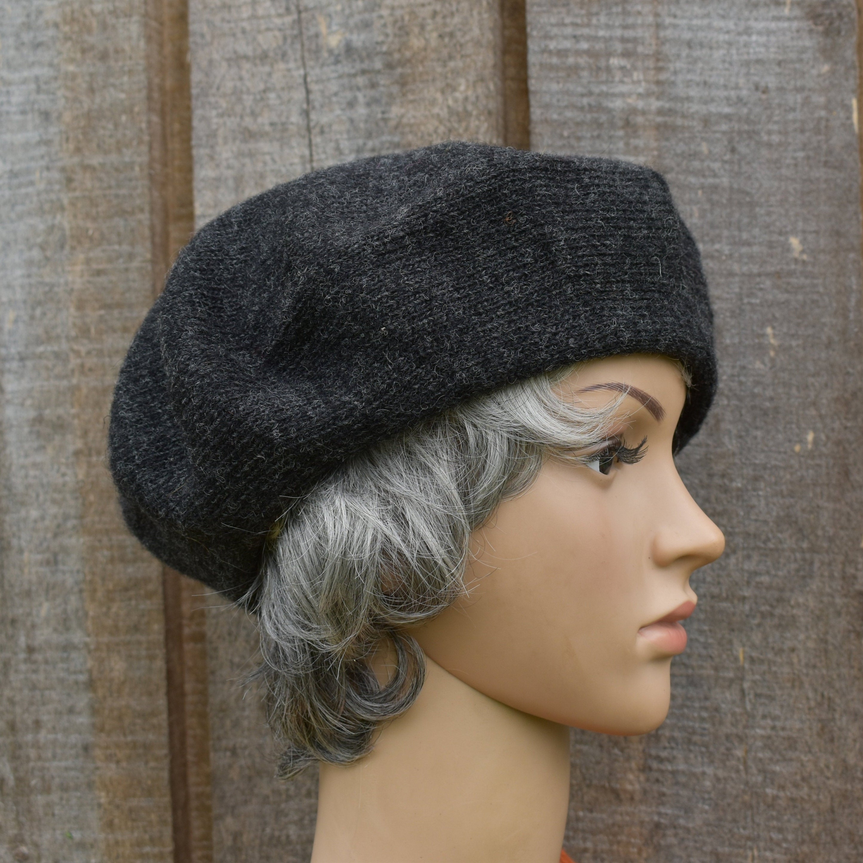 Mannequin head wearing a dark gray knit beret against a wooden background