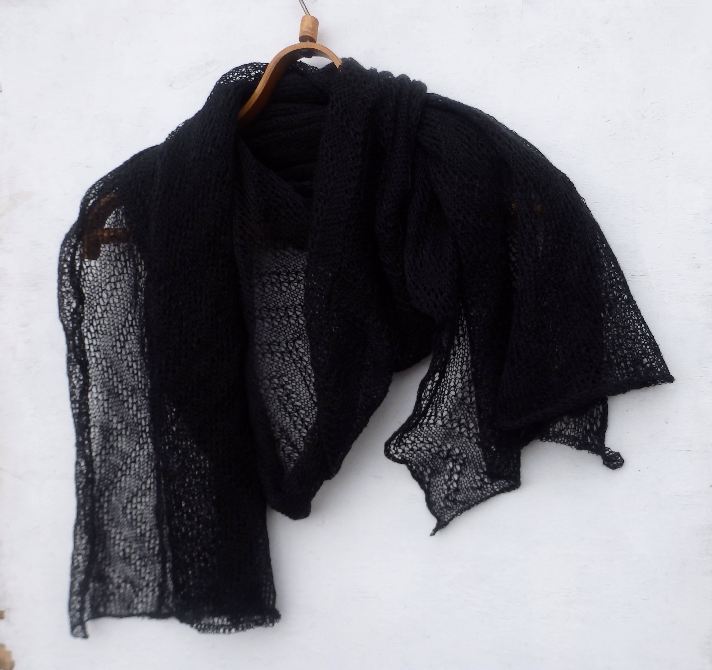 Black shawl draped over a wooden hanger on a white background