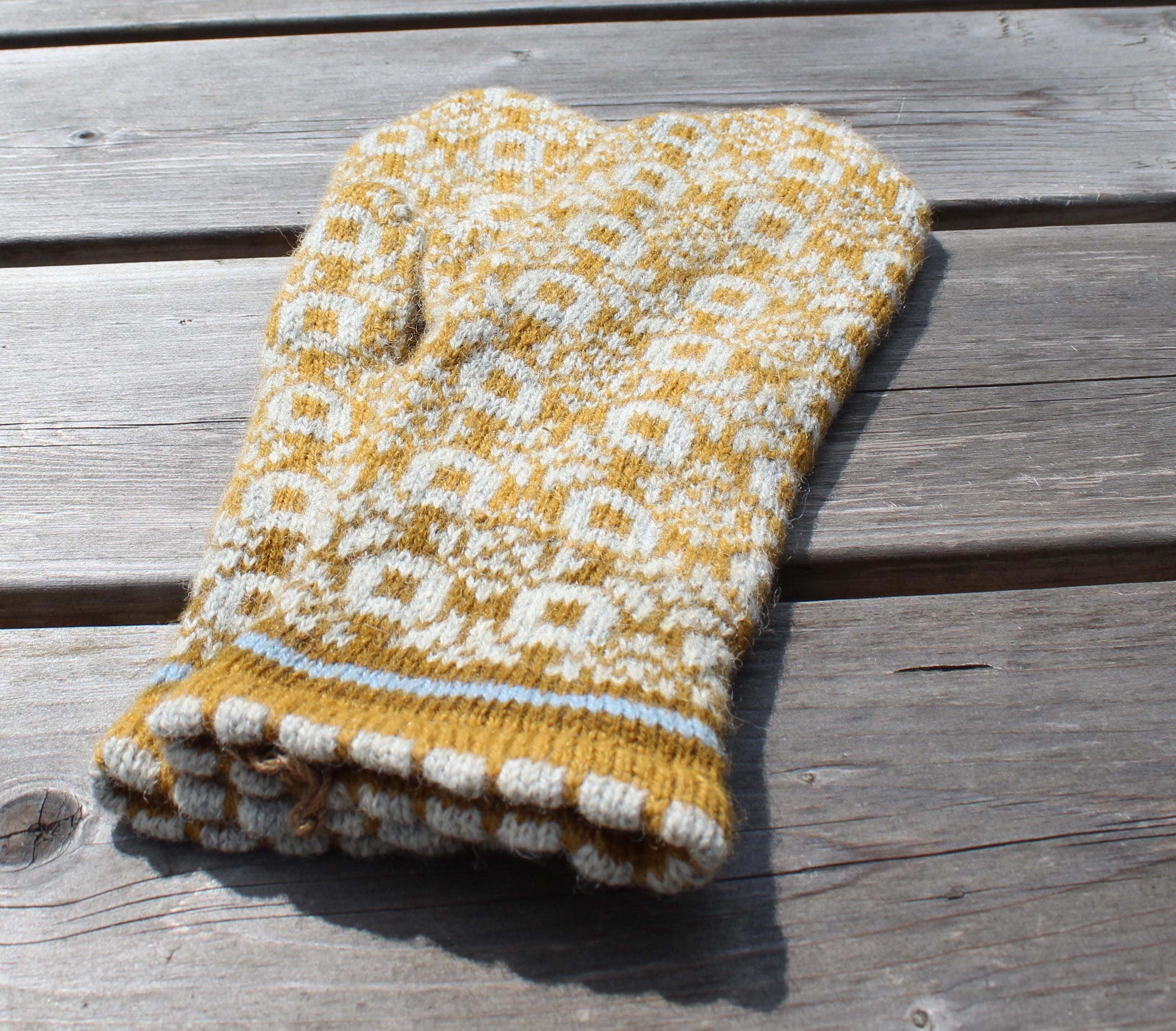 Knitted yellow and white patterned glove on a wooden surface