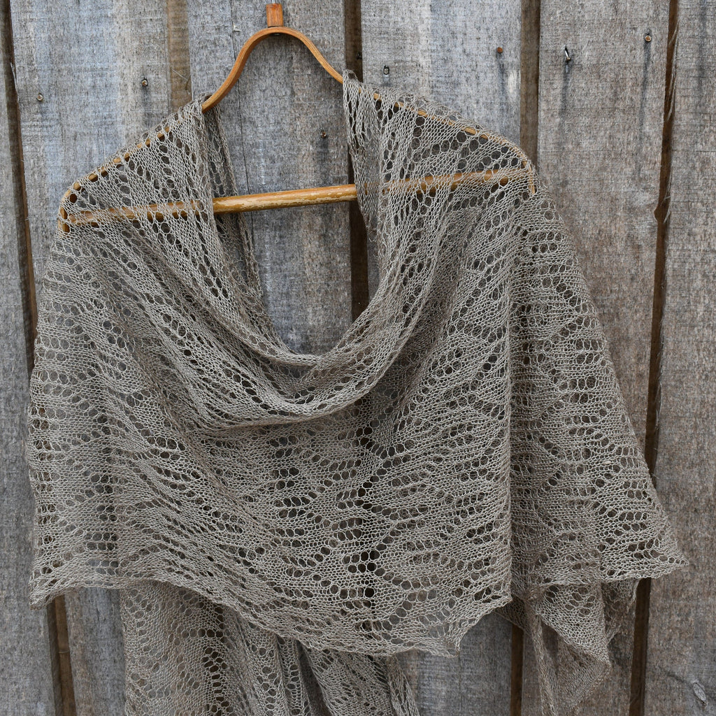 Knitted shawl on a wooden hanger against a rustic wooden background