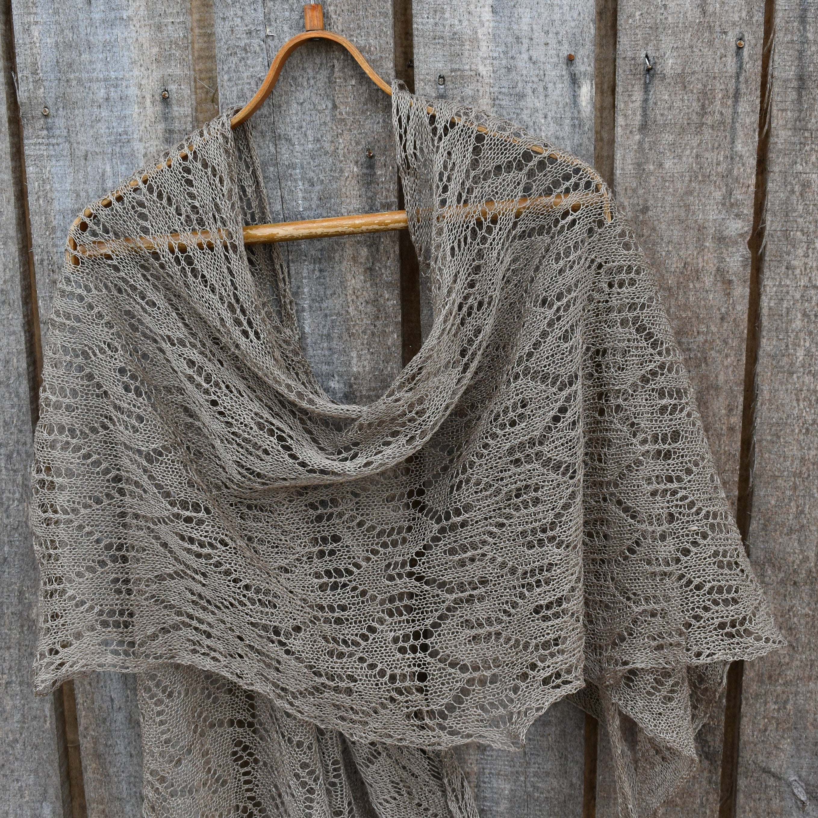 Knitted shawl on a wooden hanger against a rustic wooden background