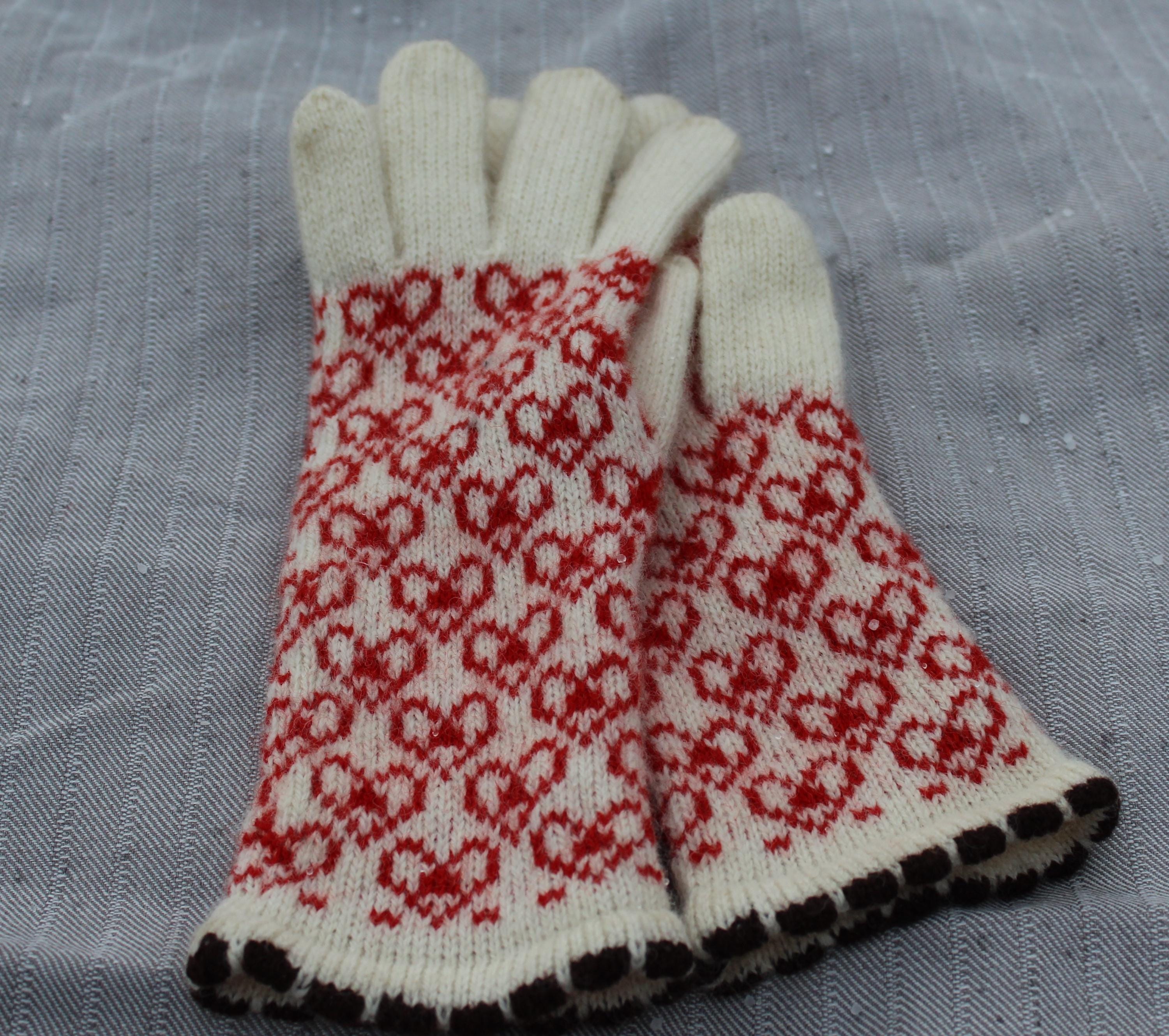 Pair of white gloves with red pattern on a gray fabric background