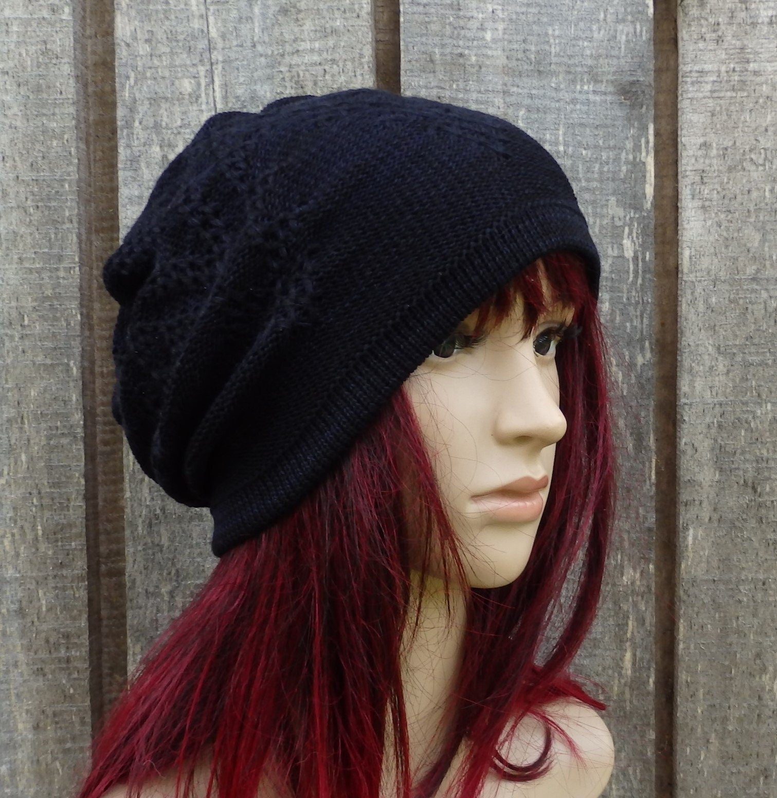 Black knit beanie on a mannequin head with red hair against a wooden panel background