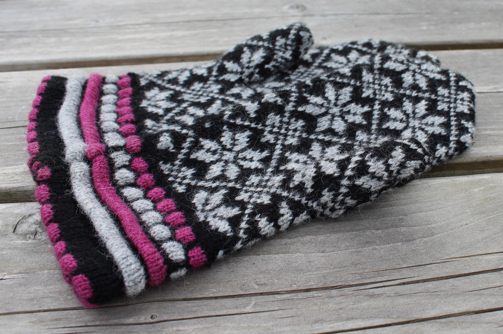Knitted glove with black, white, and pink pattern on a wooden surface