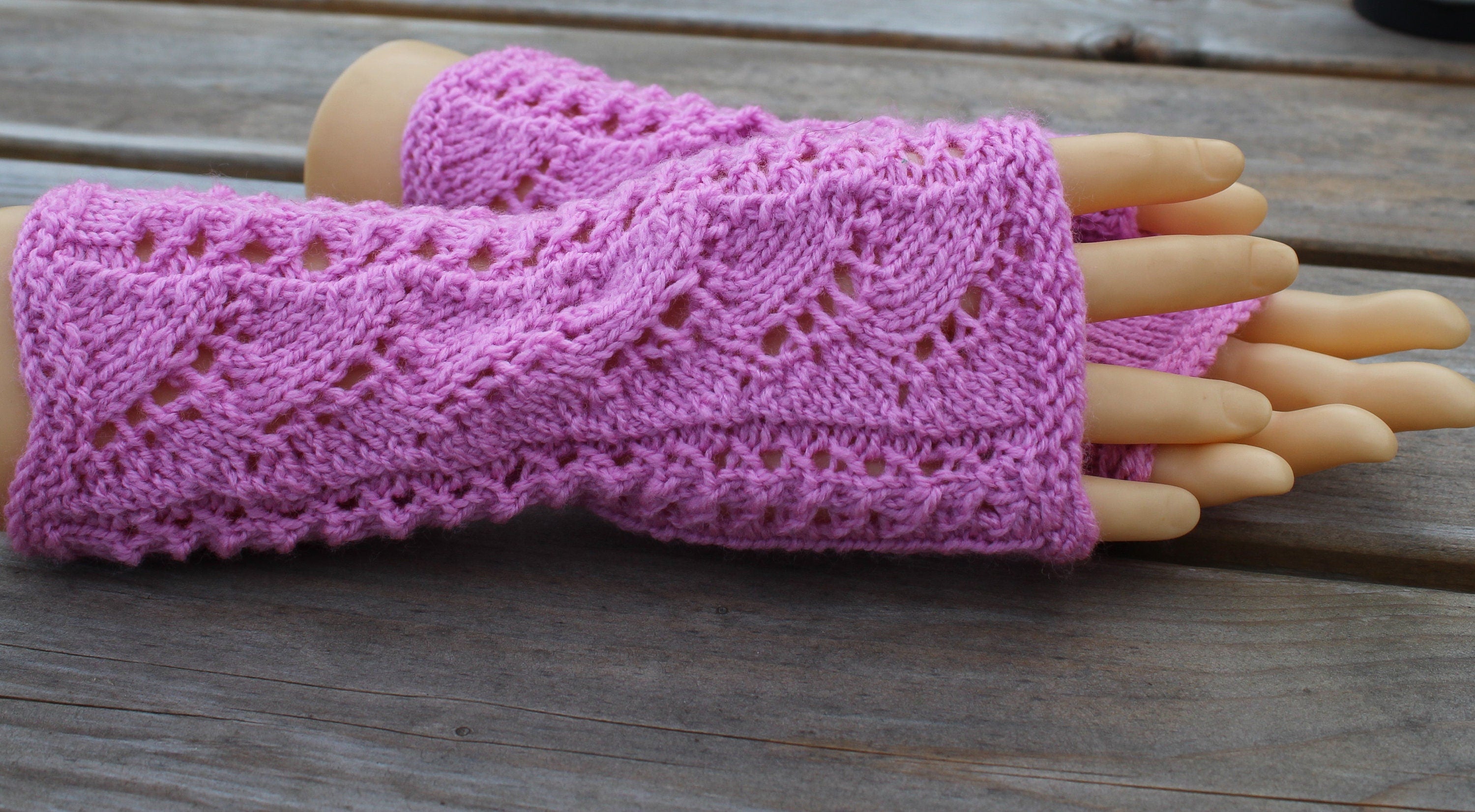 Pink knitted fingerless gloves on a wooden surface