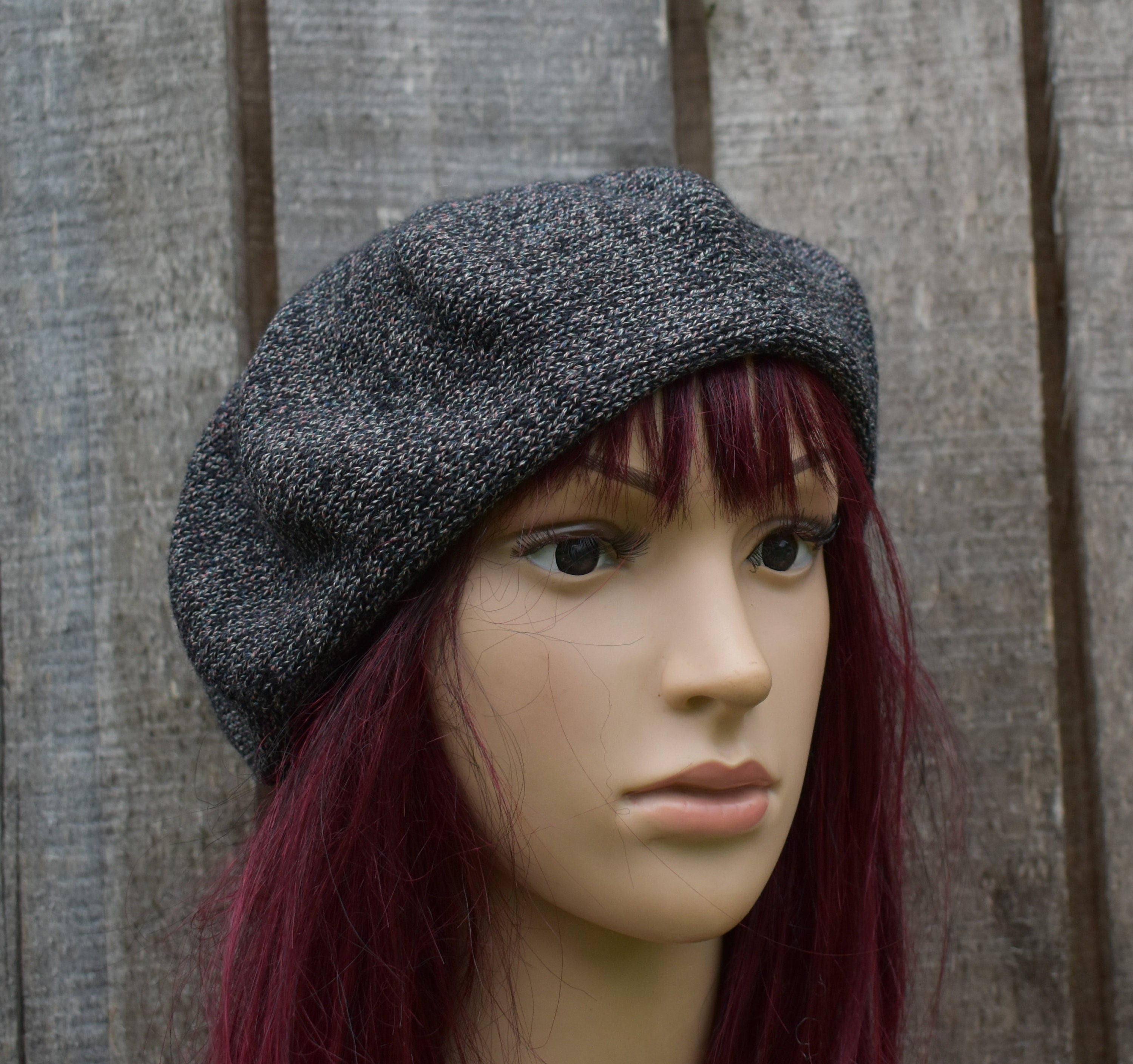Mannequin head wearing a gray knit beret against a wooden background