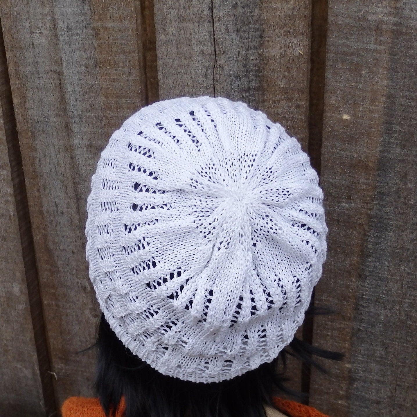 White knitted hat on a person against a wooden fence background