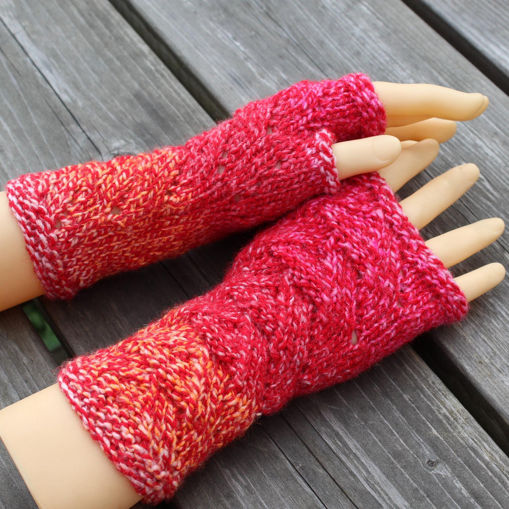 Red and pink knitted arm warmers on a mannequin arm against a wooden background