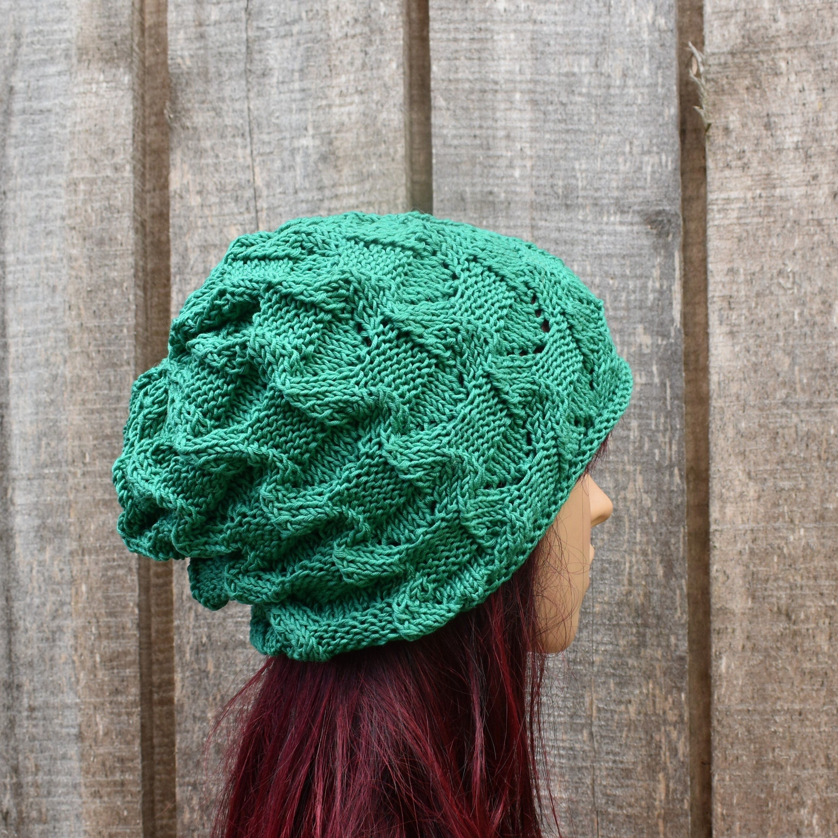 Green knitted beanie worn by a person against a wooden background