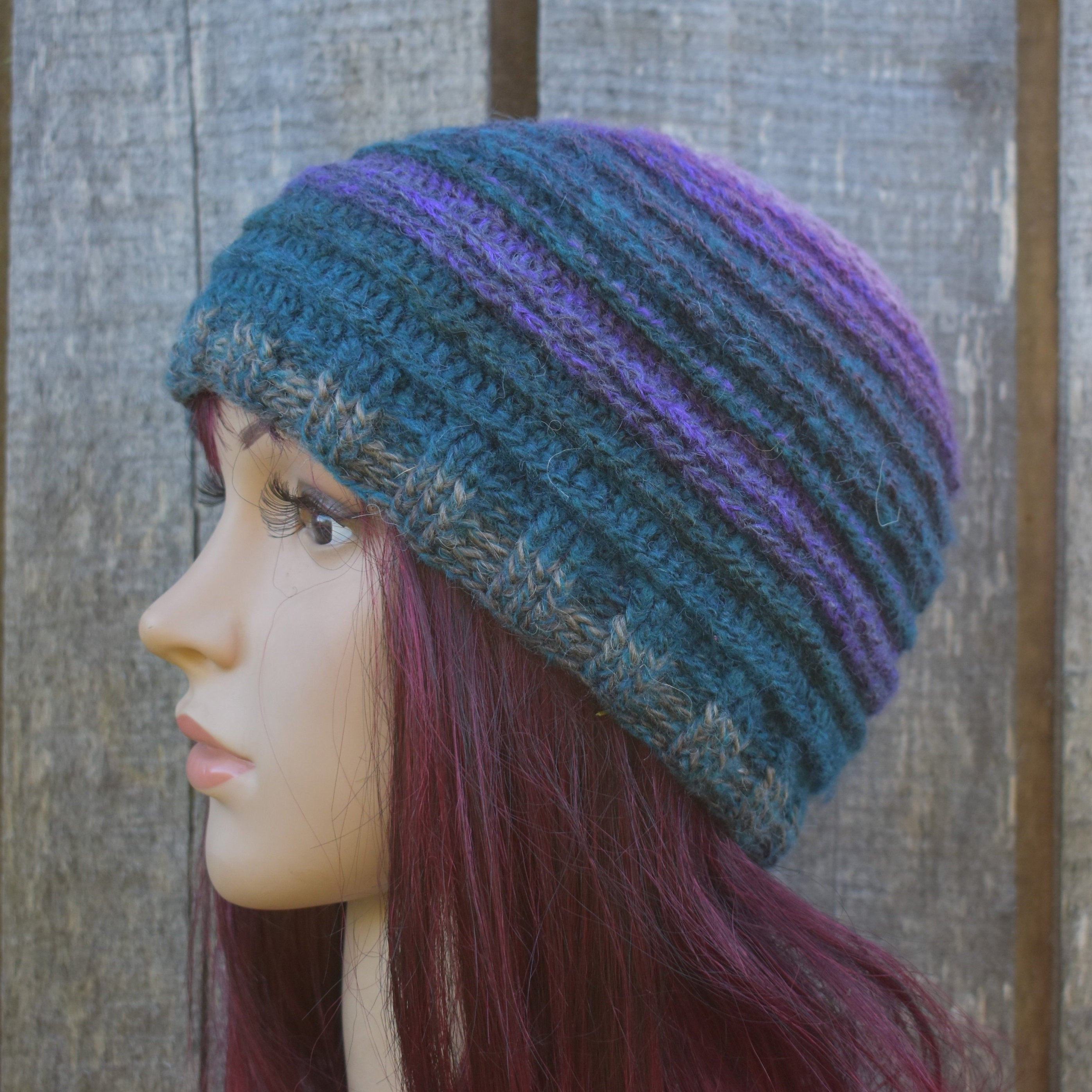 Crocheted beanie with blue and purple stripes on a mannequin head against a wooden background