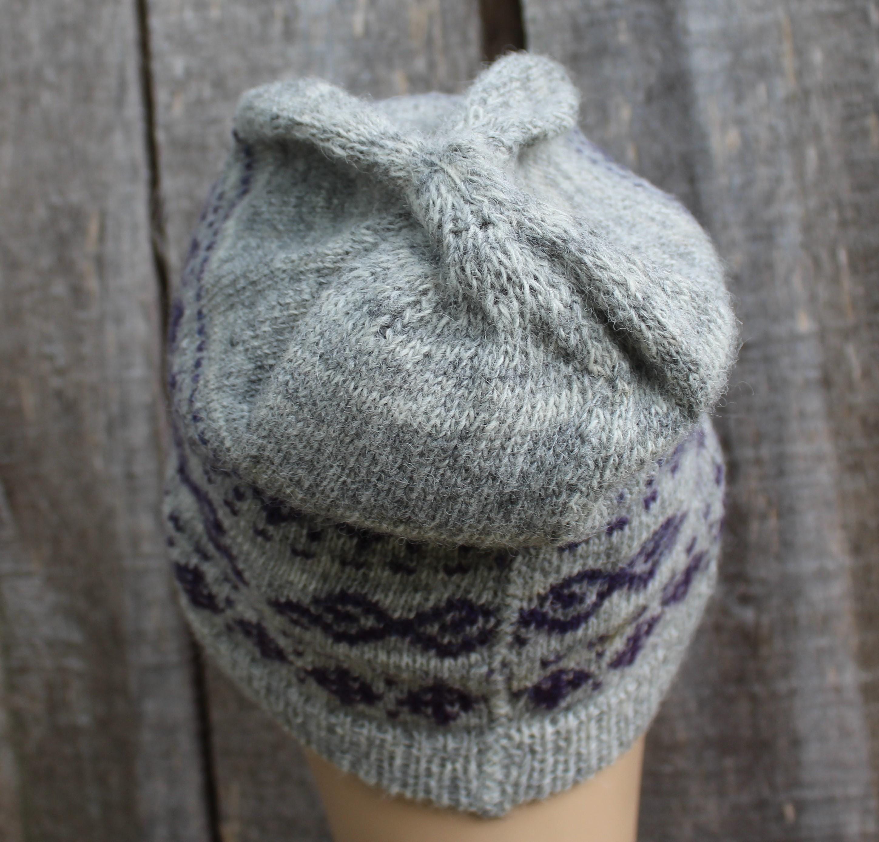 Gray knitted hat with purple pattern on a wooden background