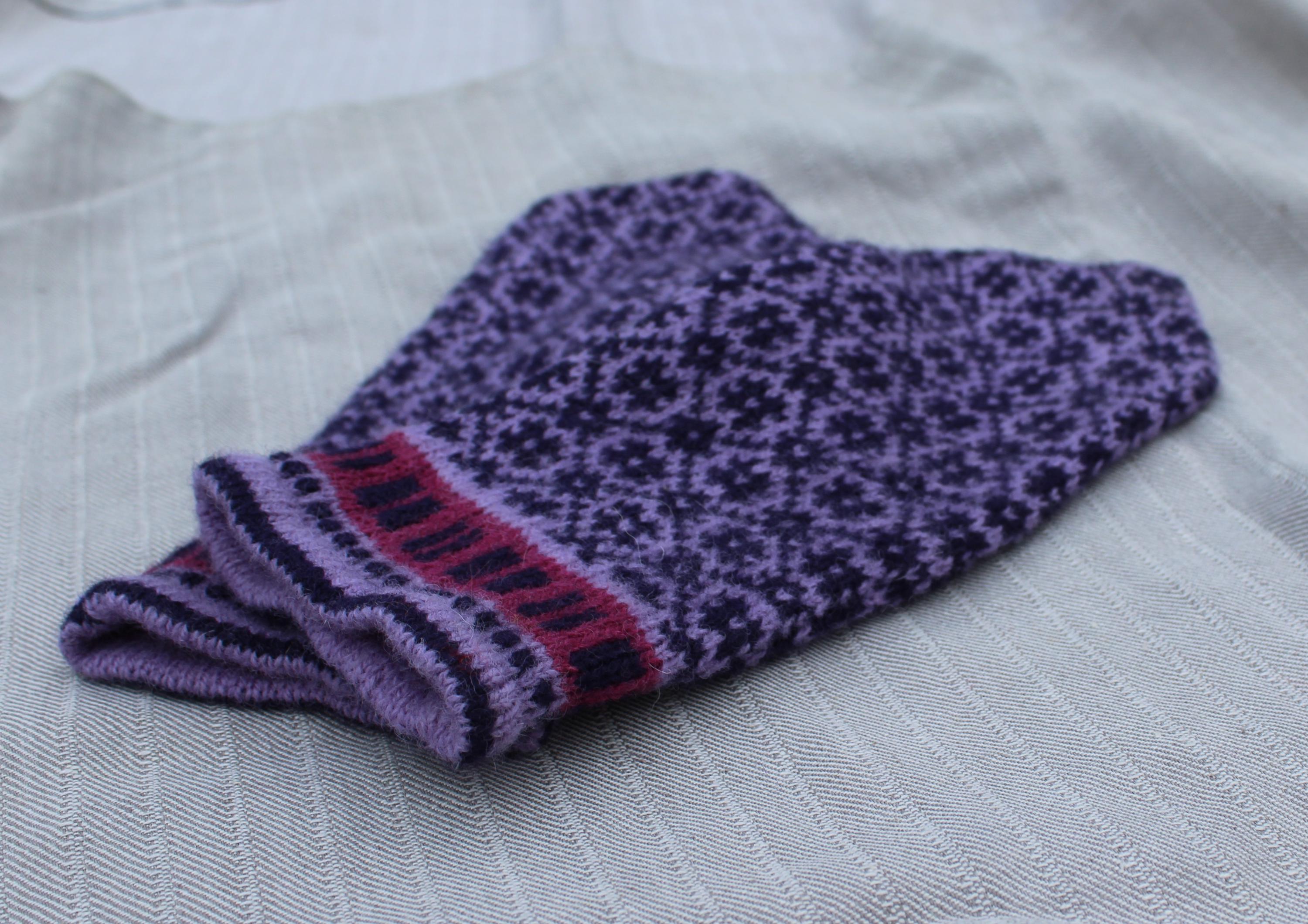 Pair of purple knitted socks with a pattern on a light fabric background