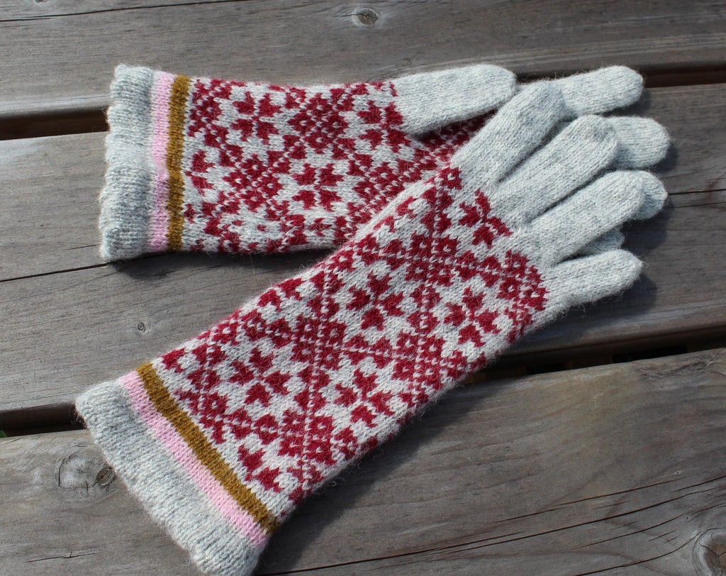 Pair of knitted gloves with a red and white pattern on a wooden surface