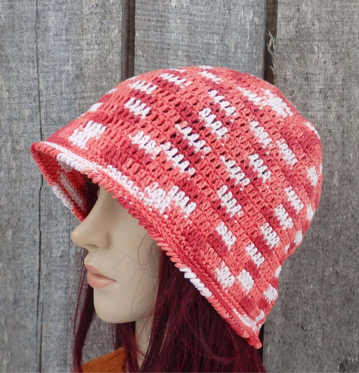 Pink and white striped crochet hat on a mannequin head against a wooden background