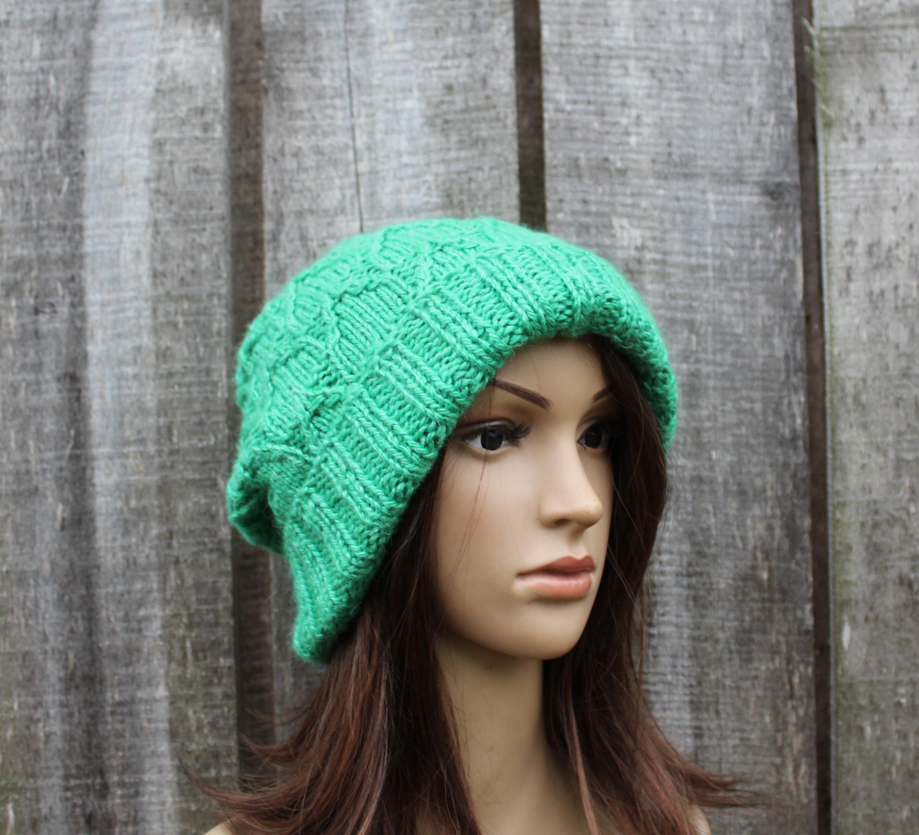 Green knitted beanie on a mannequin head against a wooden background