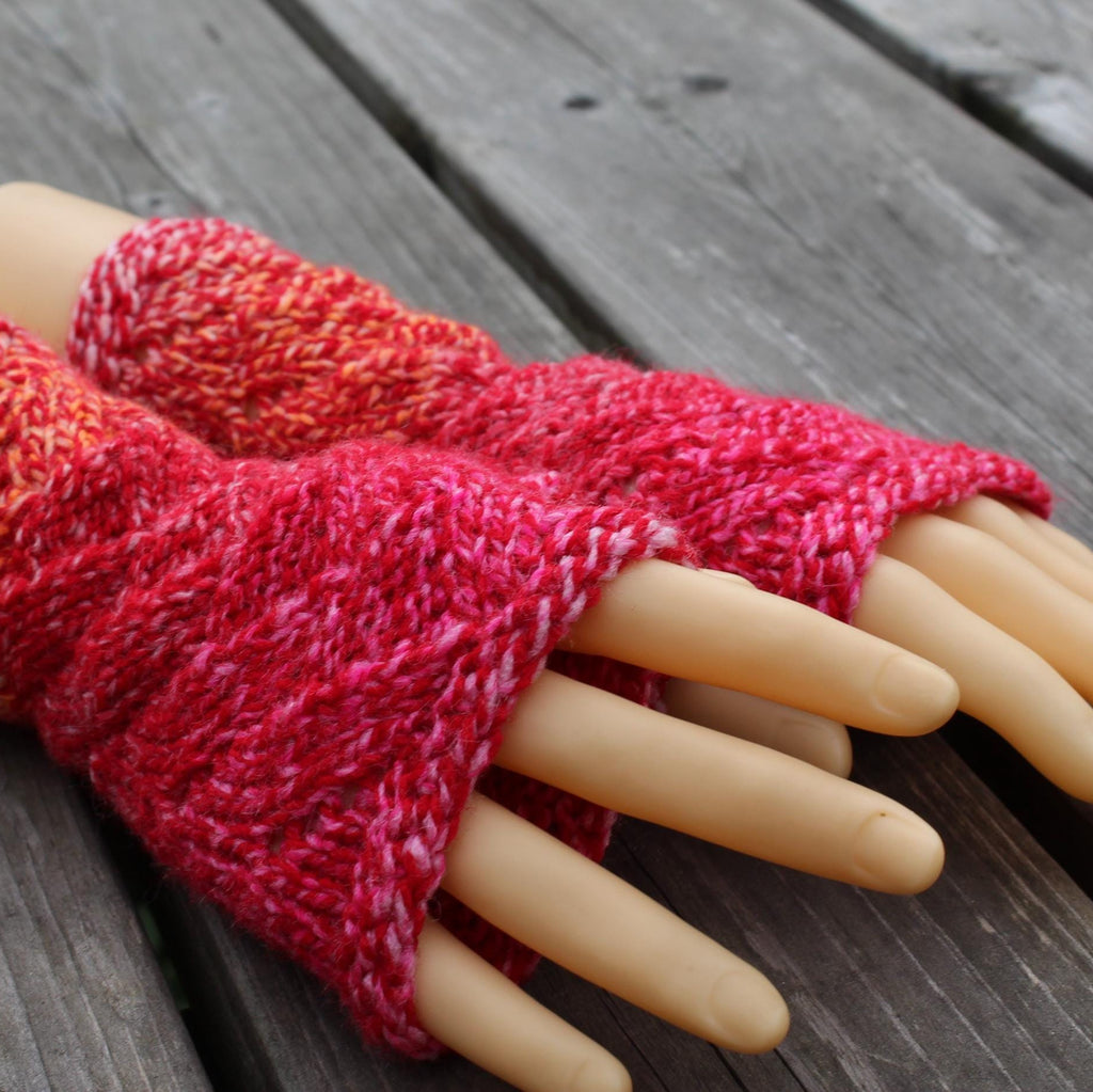 Red knitted wrist warmers on a mannequin hand against a wooden background