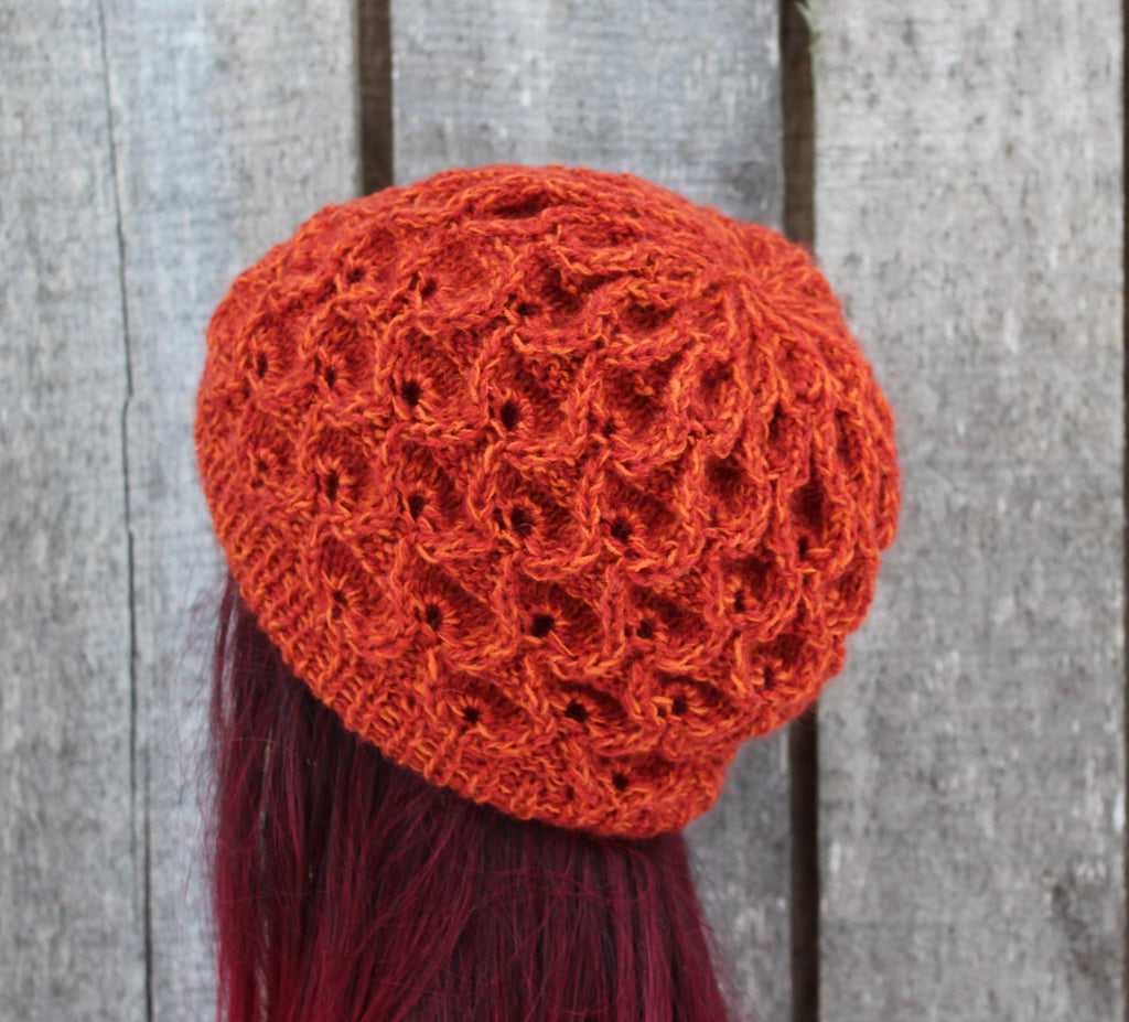 Orange knitted hat with tassel on a wooden background