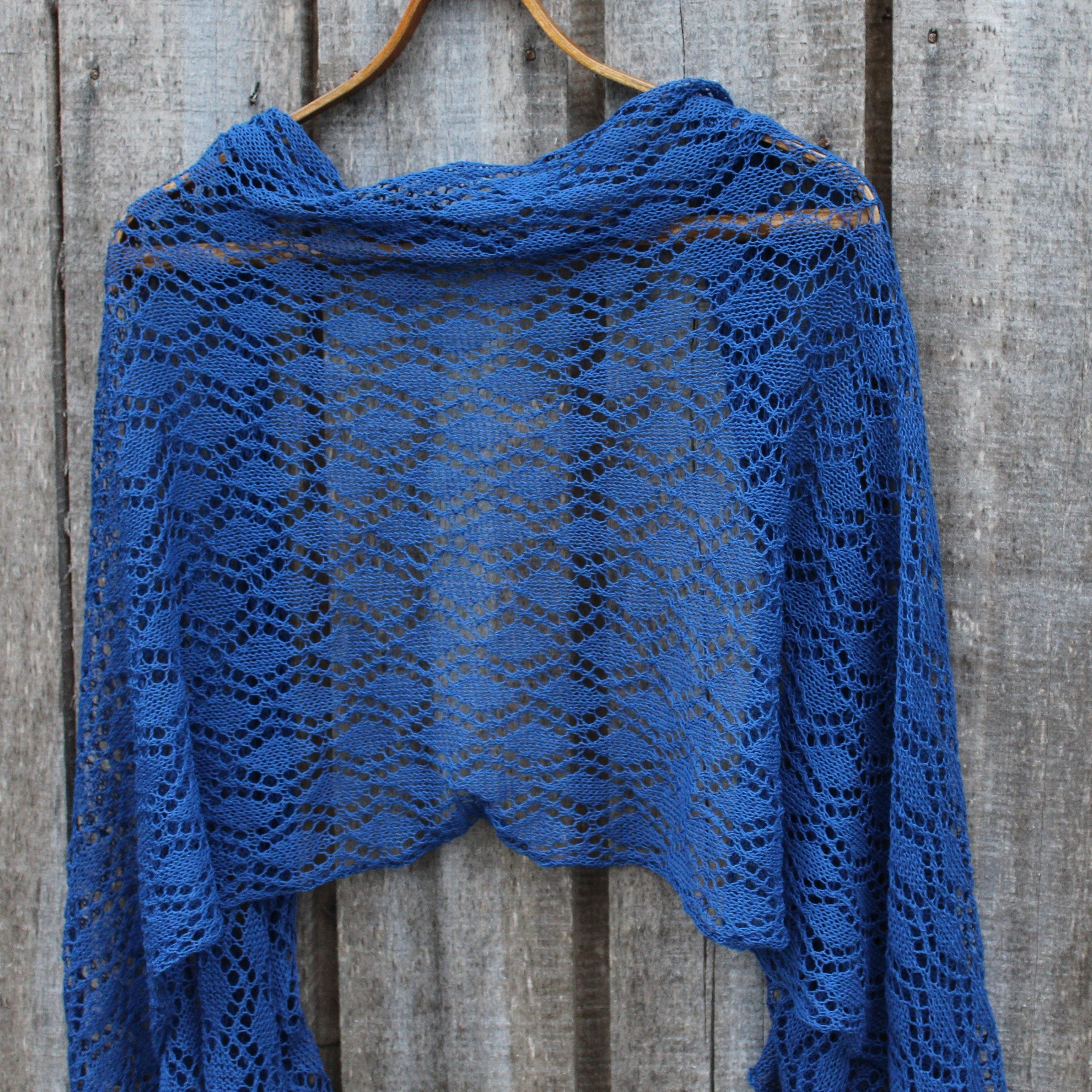 Blue knitted shawl on a wooden hanger against a wooden background