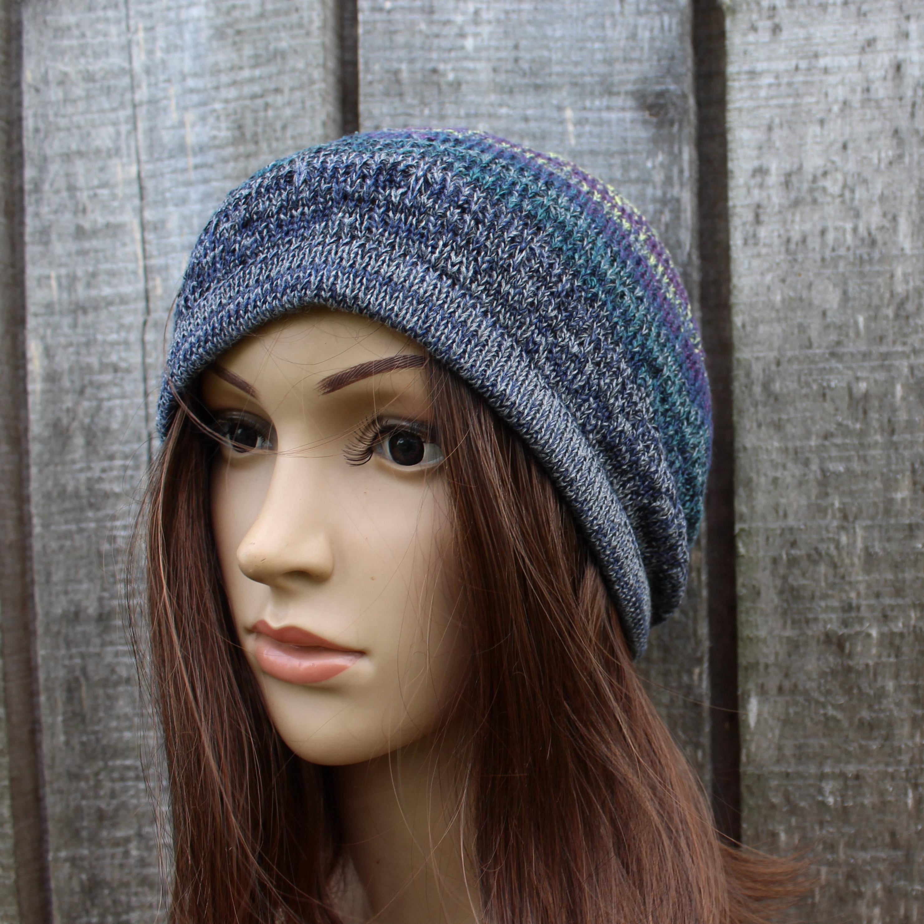 Mannequin head wearing a blue knit beanie against a wooden fence background