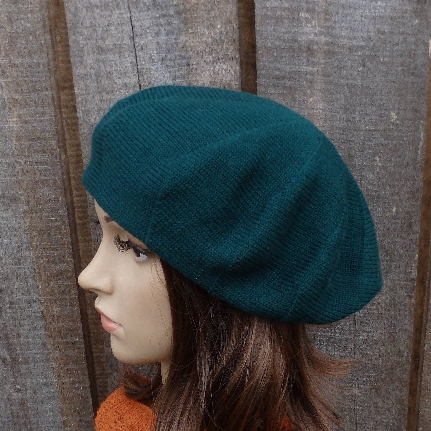 Teal beret worn by a mannequin head against a wooden background
