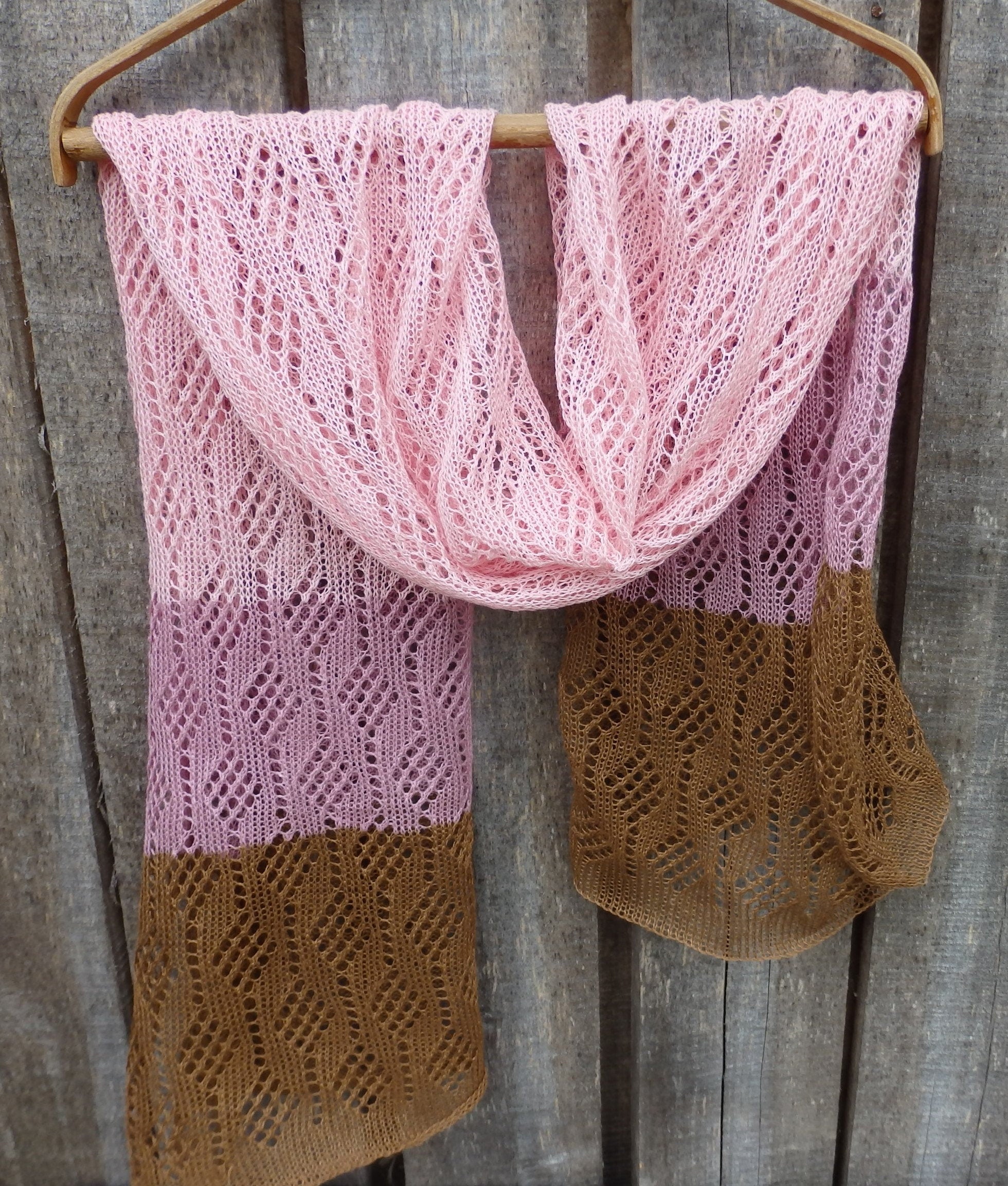 Pink and brown knitted scarf on a wooden hanger against a wooden background
