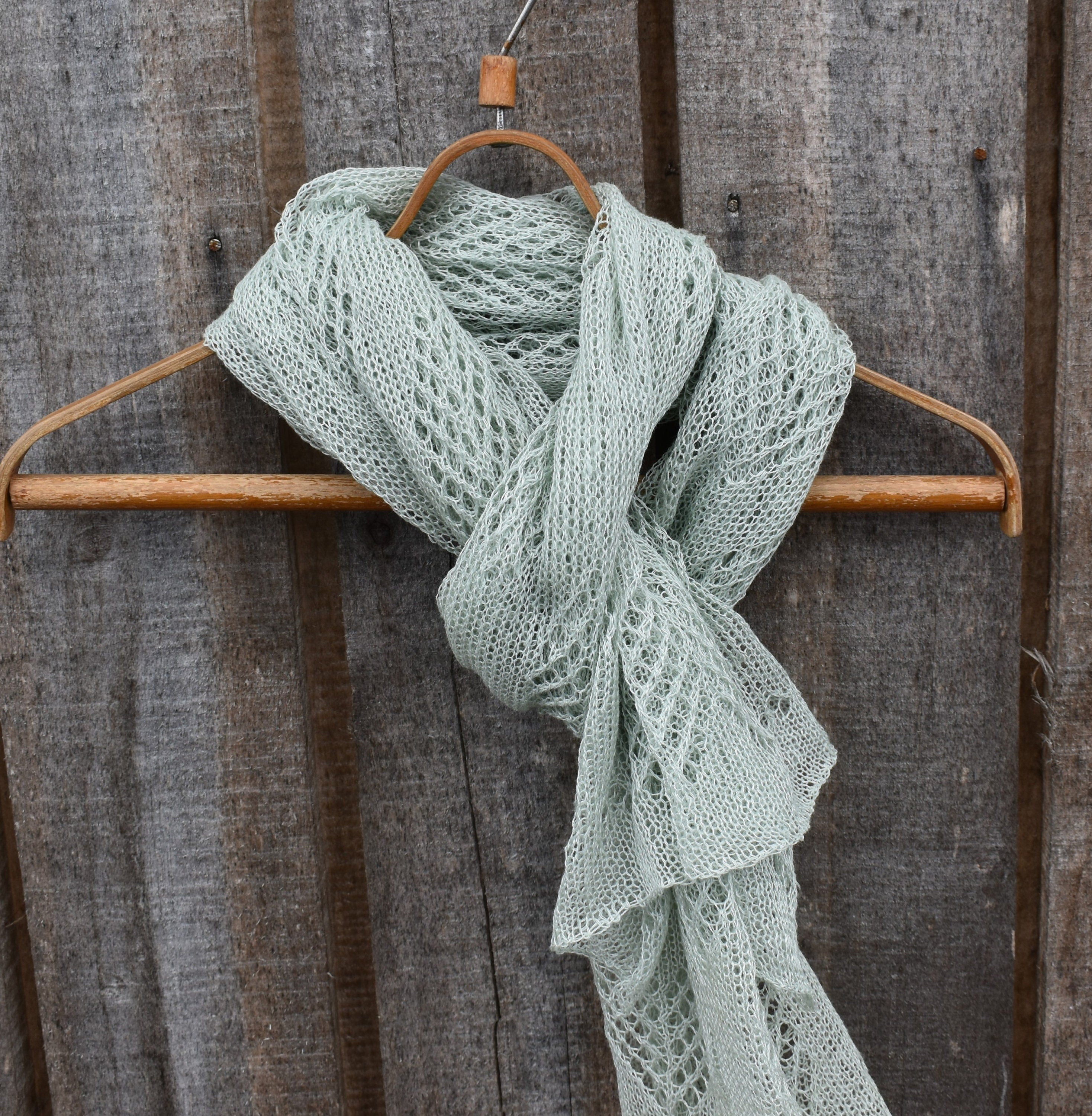 Knitted green scarf on a wooden hanger against a rustic wooden background