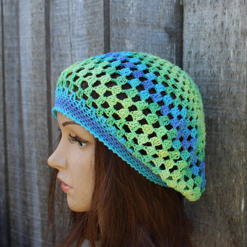 Mannequin head wearing a green and blue crocheted hat against a wooden background