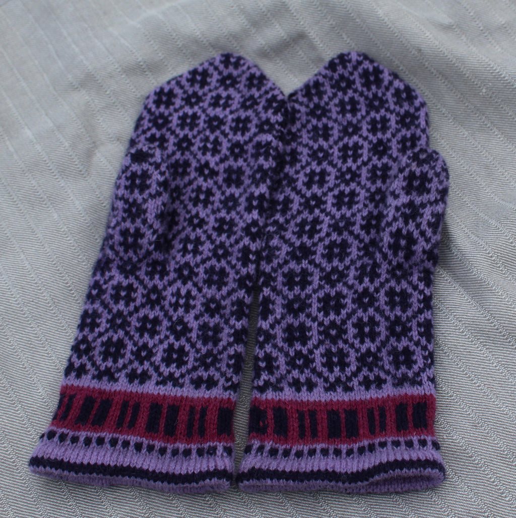 Knitted purple mitten with black pattern on a white fabric background