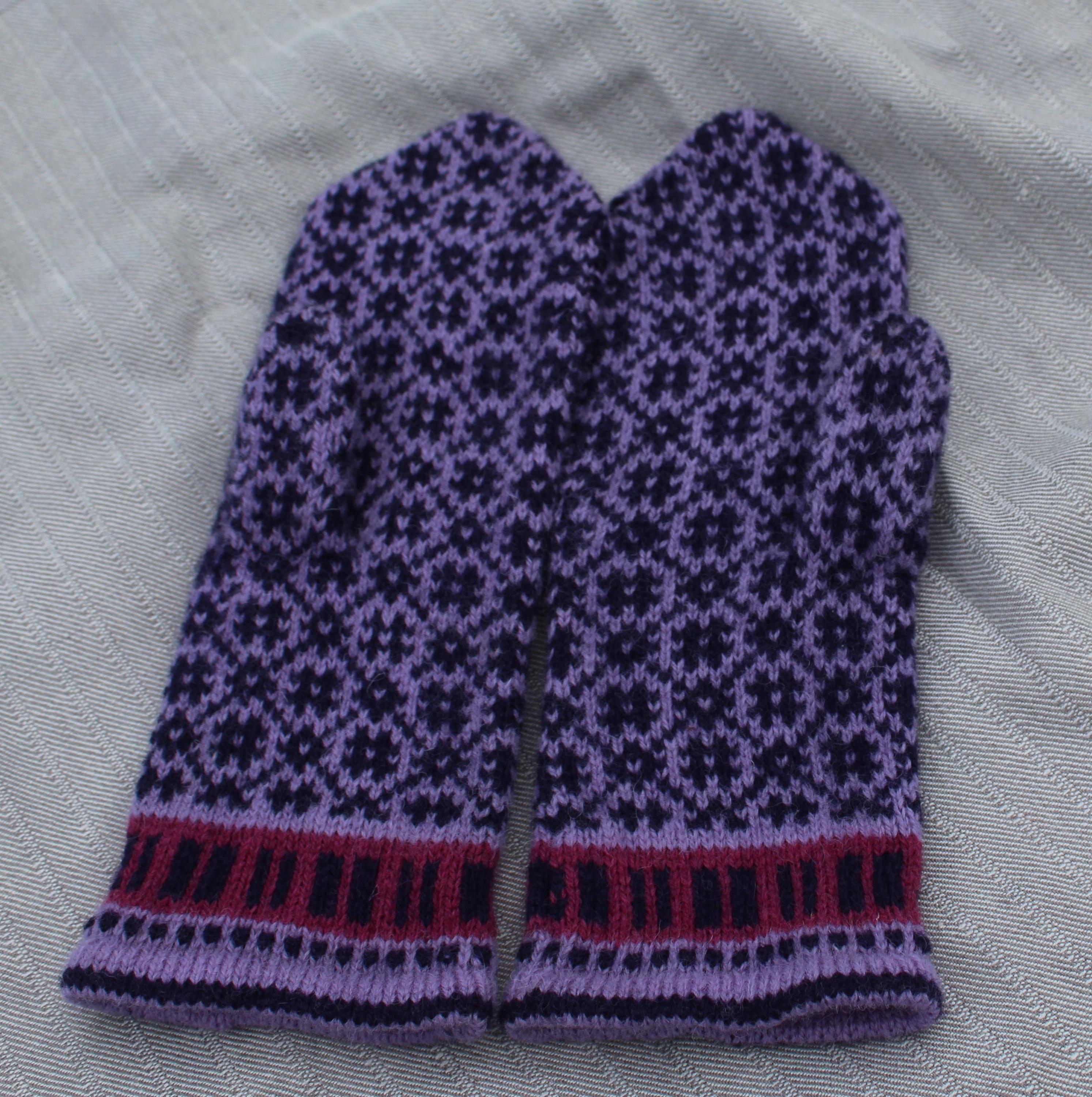 Knitted purple mitten with black pattern on a white fabric background