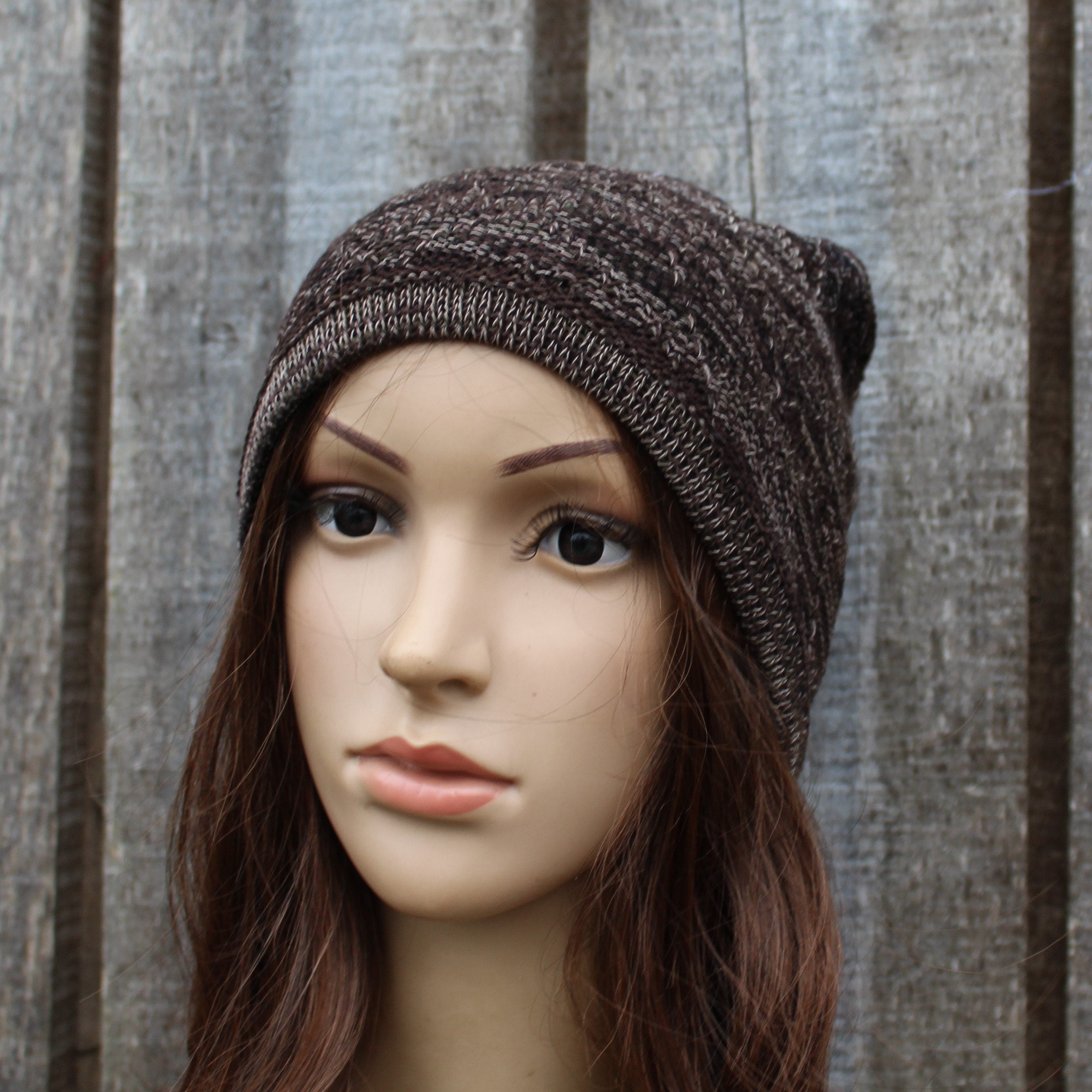 Mannequin head wearing a brown knit beanie against a wooden panel background