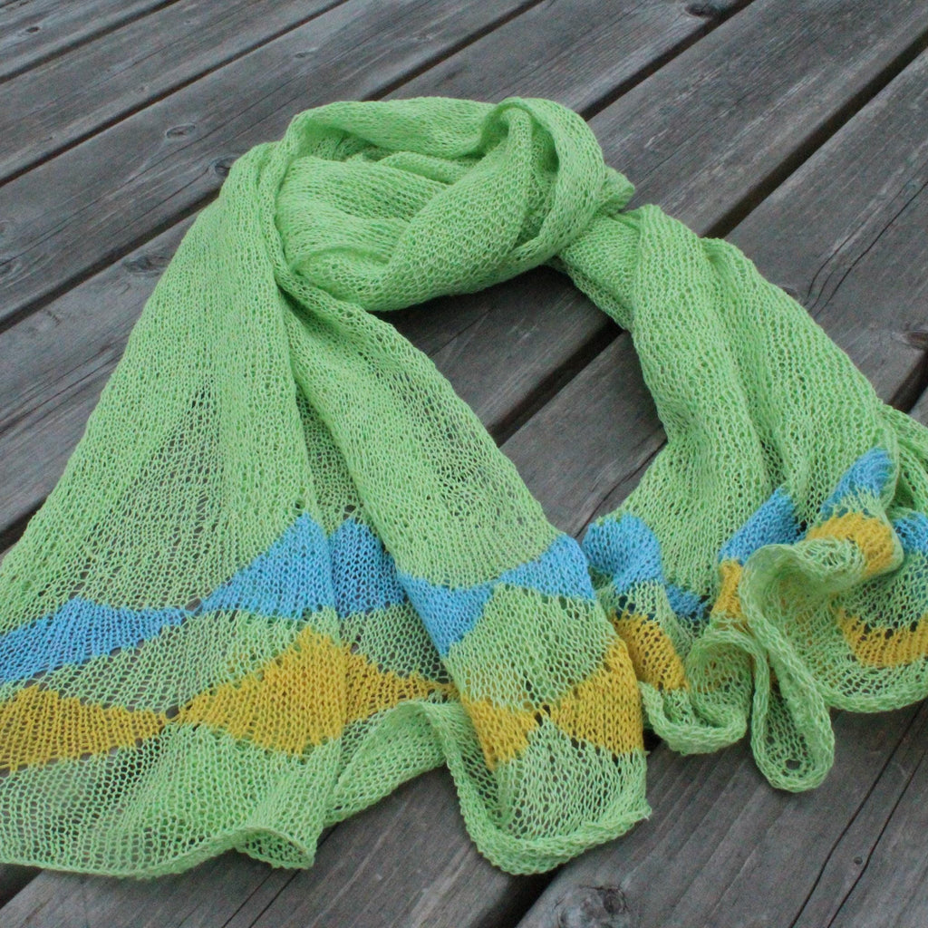 Green knitted shawl with blue and yellow pattern on a wooden surface