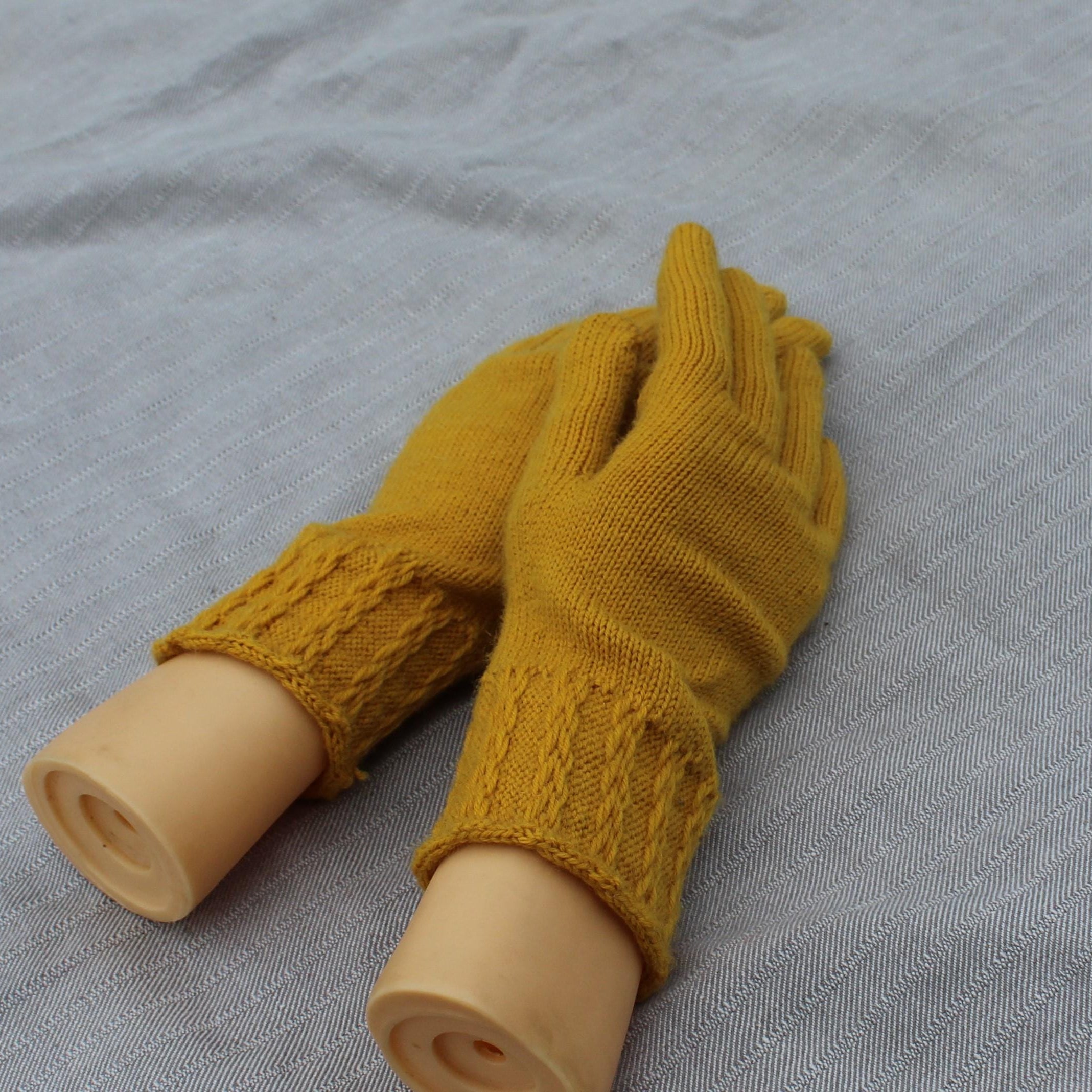 Mustard yellow fingerless gloves on a mannequin arm against a gray background
