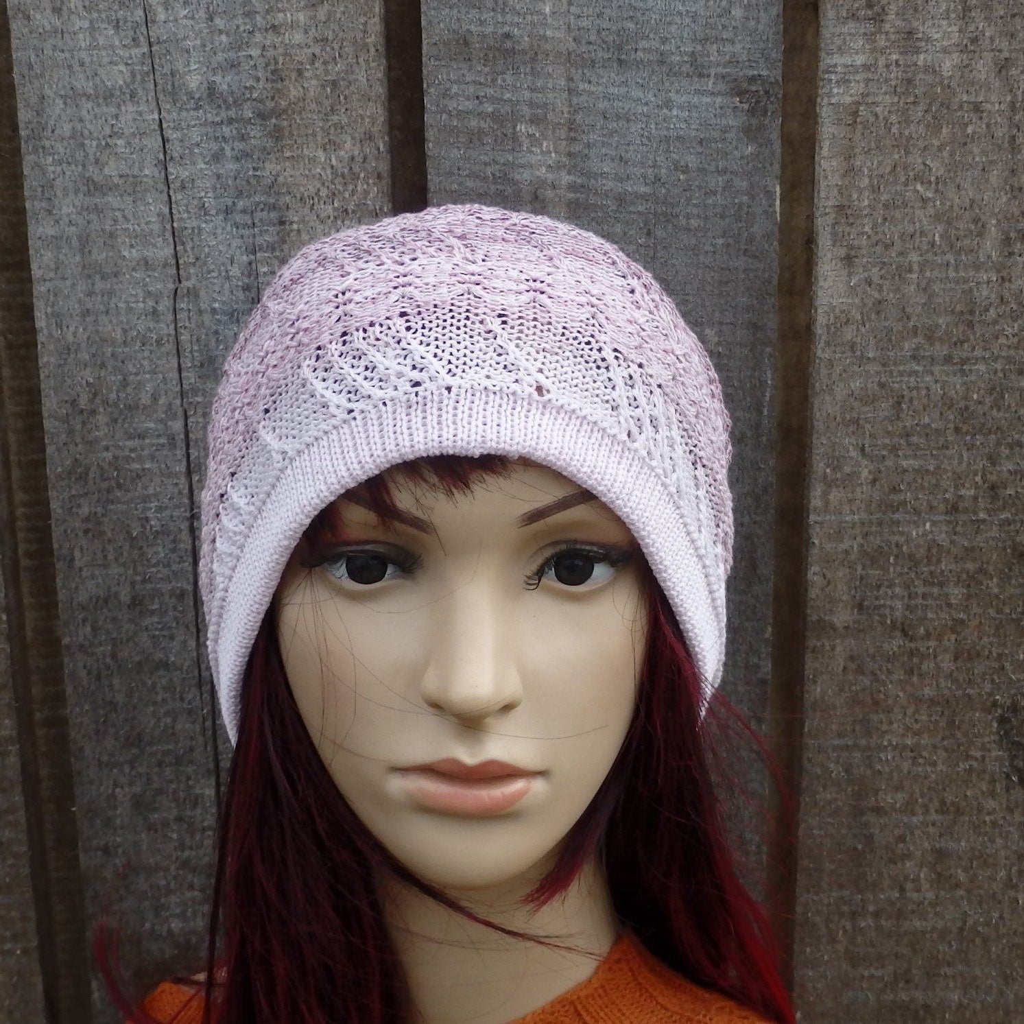 Mannequin head wearing a light purple knitted hat against a wooden background