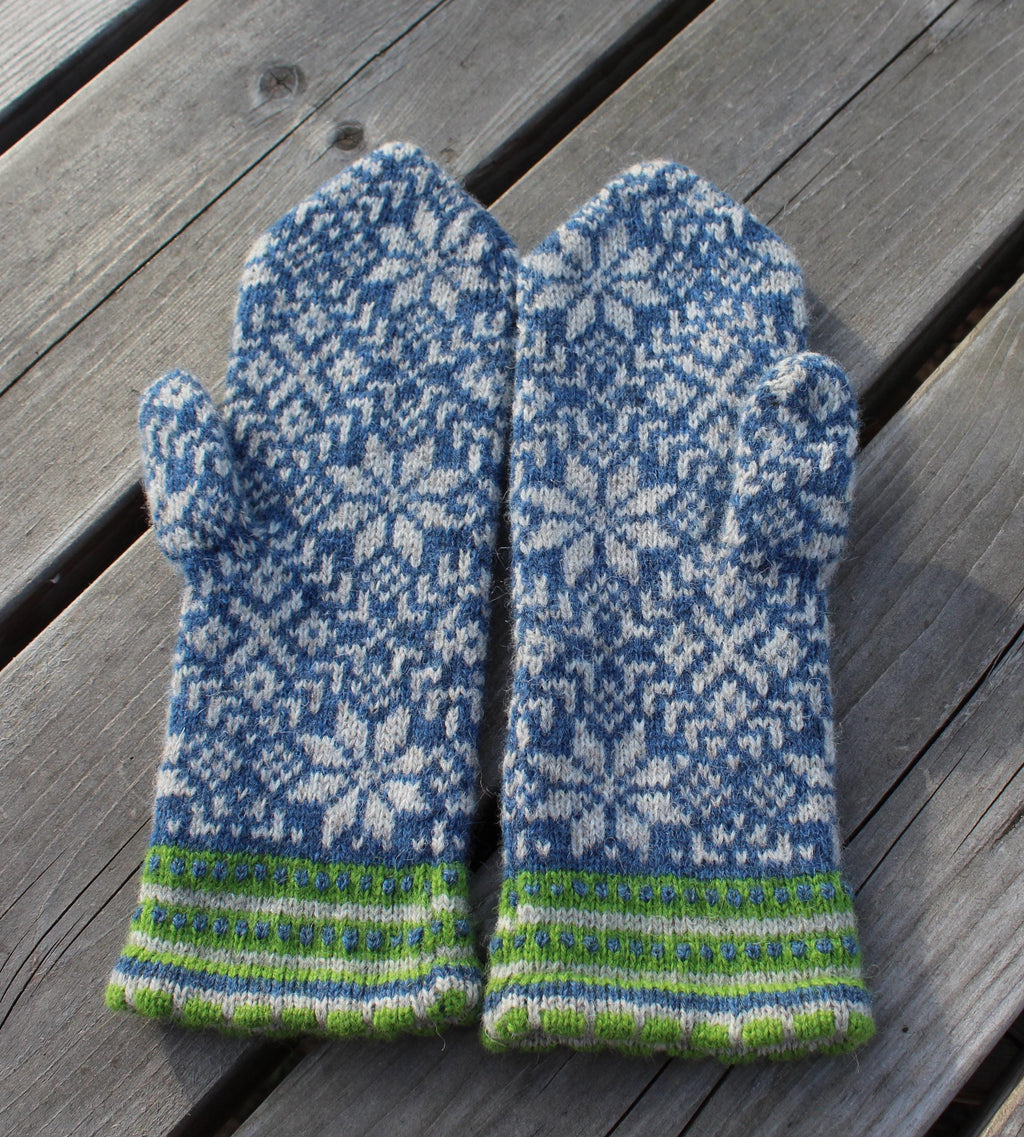 Pair of blue and gray patterned mittens with green accents on a wooden surface
