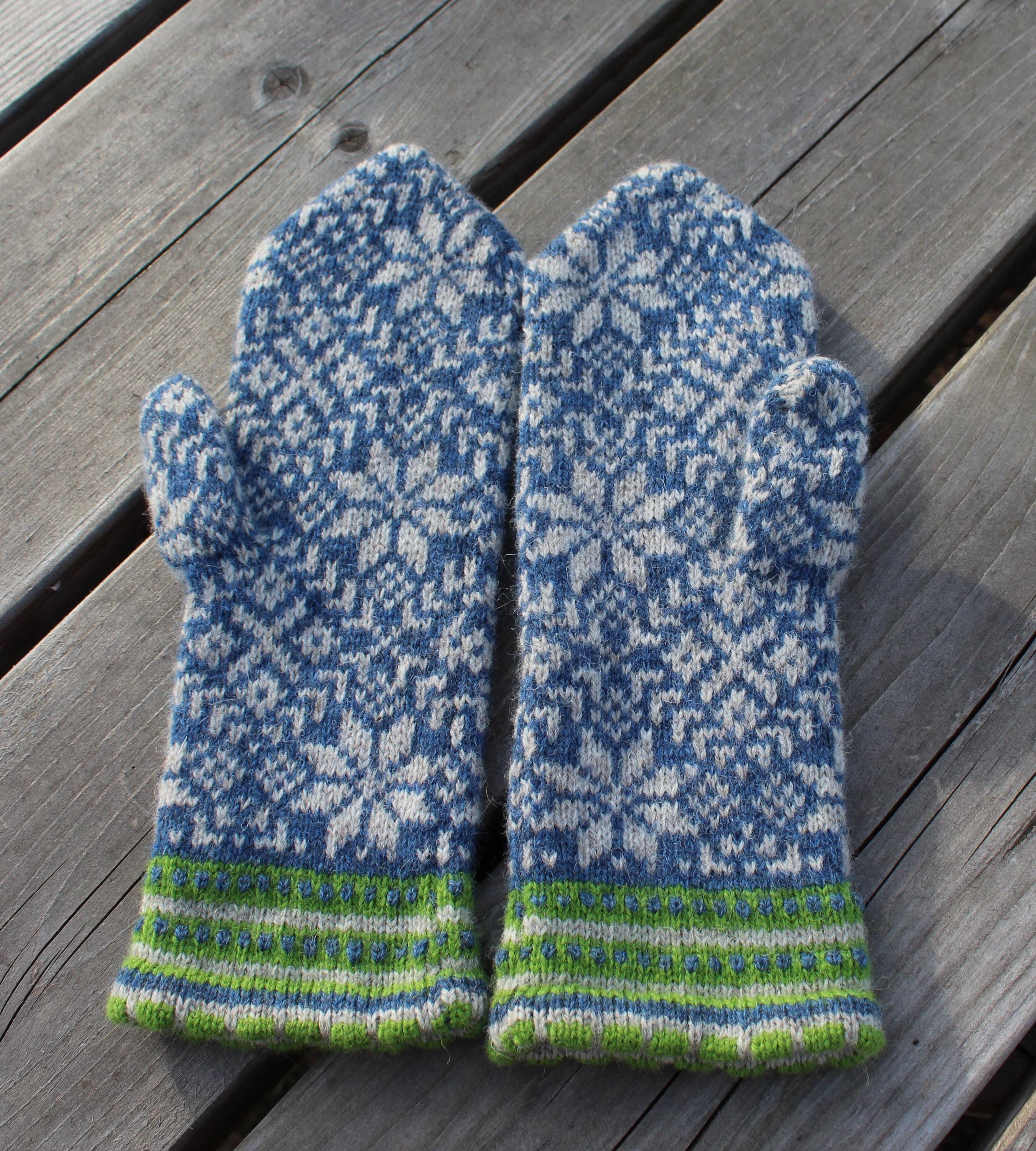 Pair of blue and gray patterned mittens with green accents on a wooden surface