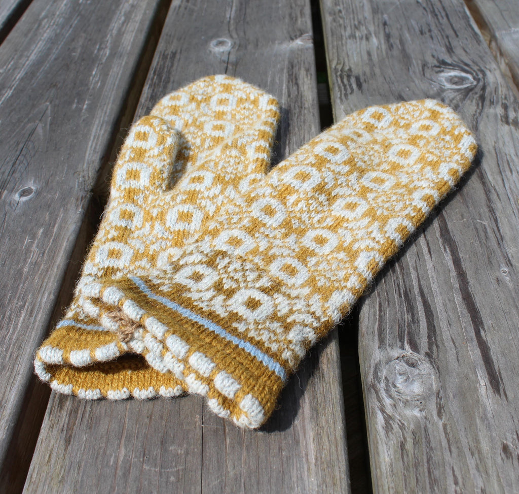 Knitted yellow and white patterned mittens on a wooden surface