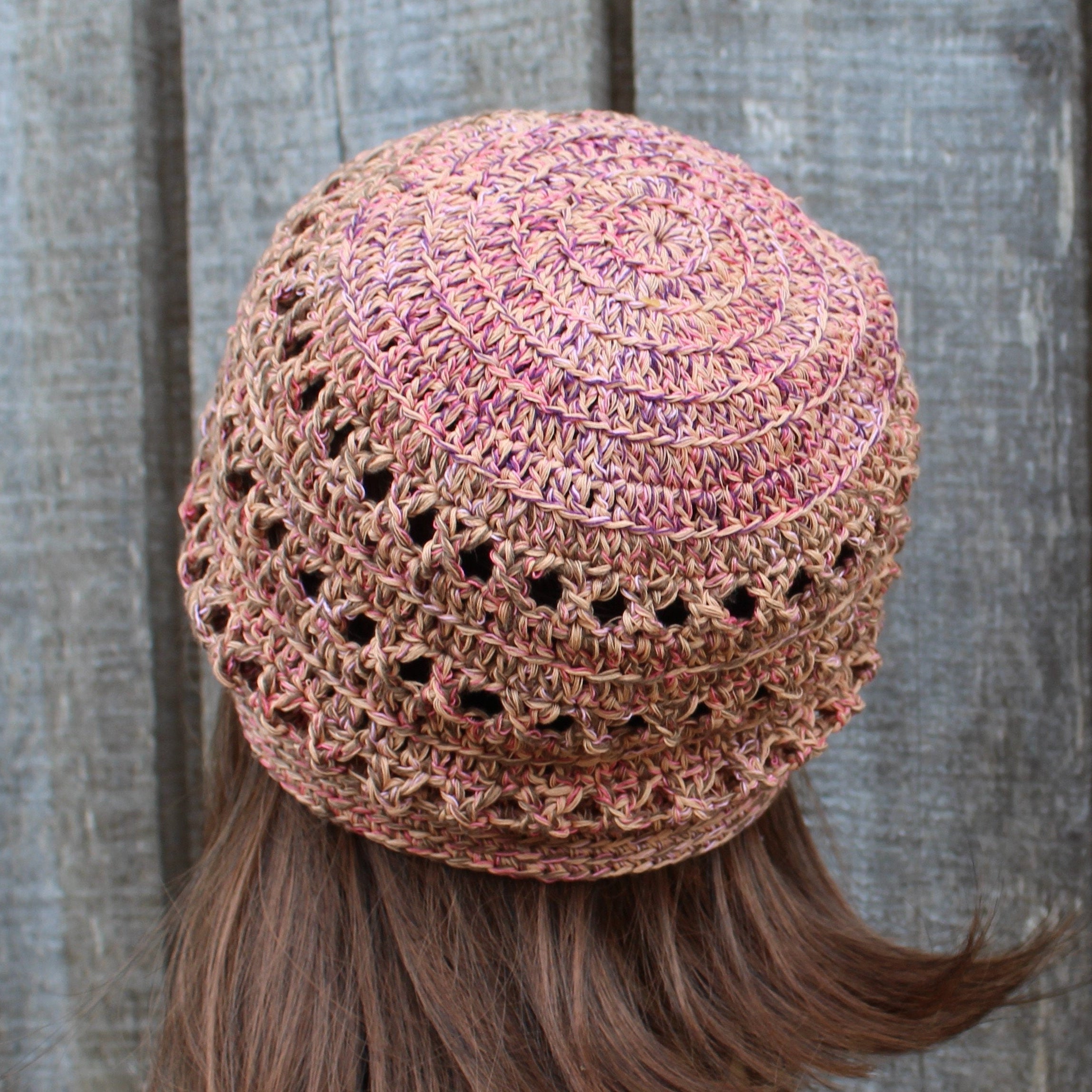 Crocheted hat with a textured pattern worn by a person with long hair against a wooden background