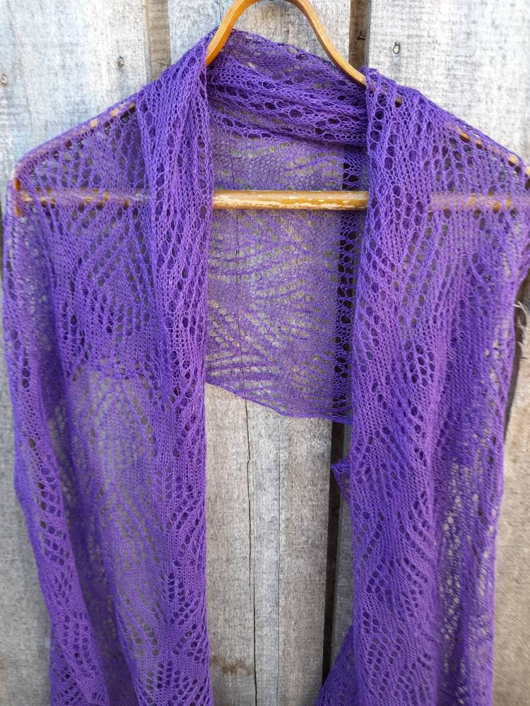 Purple knitted shawl on a wooden hanger against a wooden background